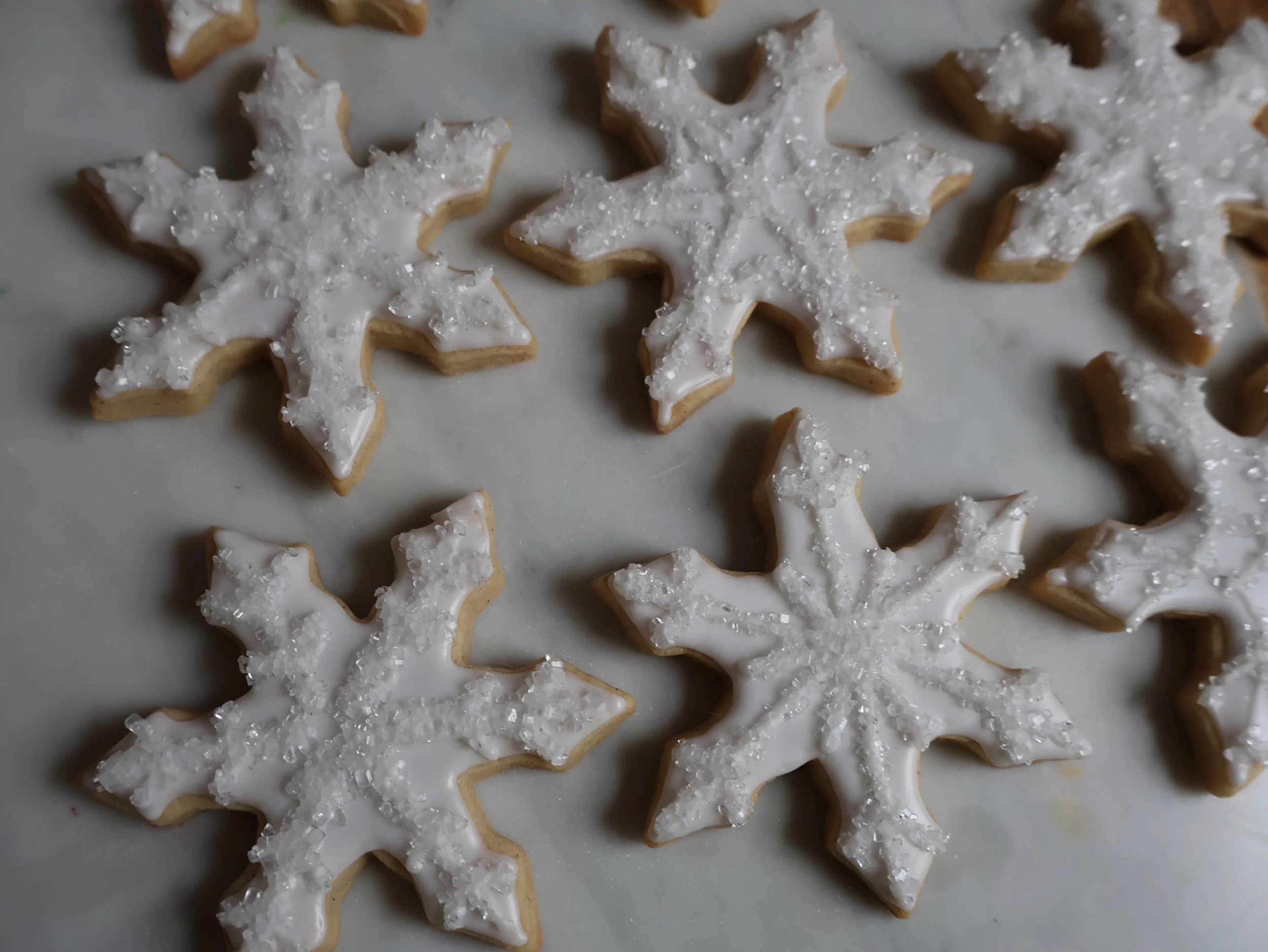 Christmas tree-shaped cookies with white icing and sugar crystals on top, arranged on a baking sheet.