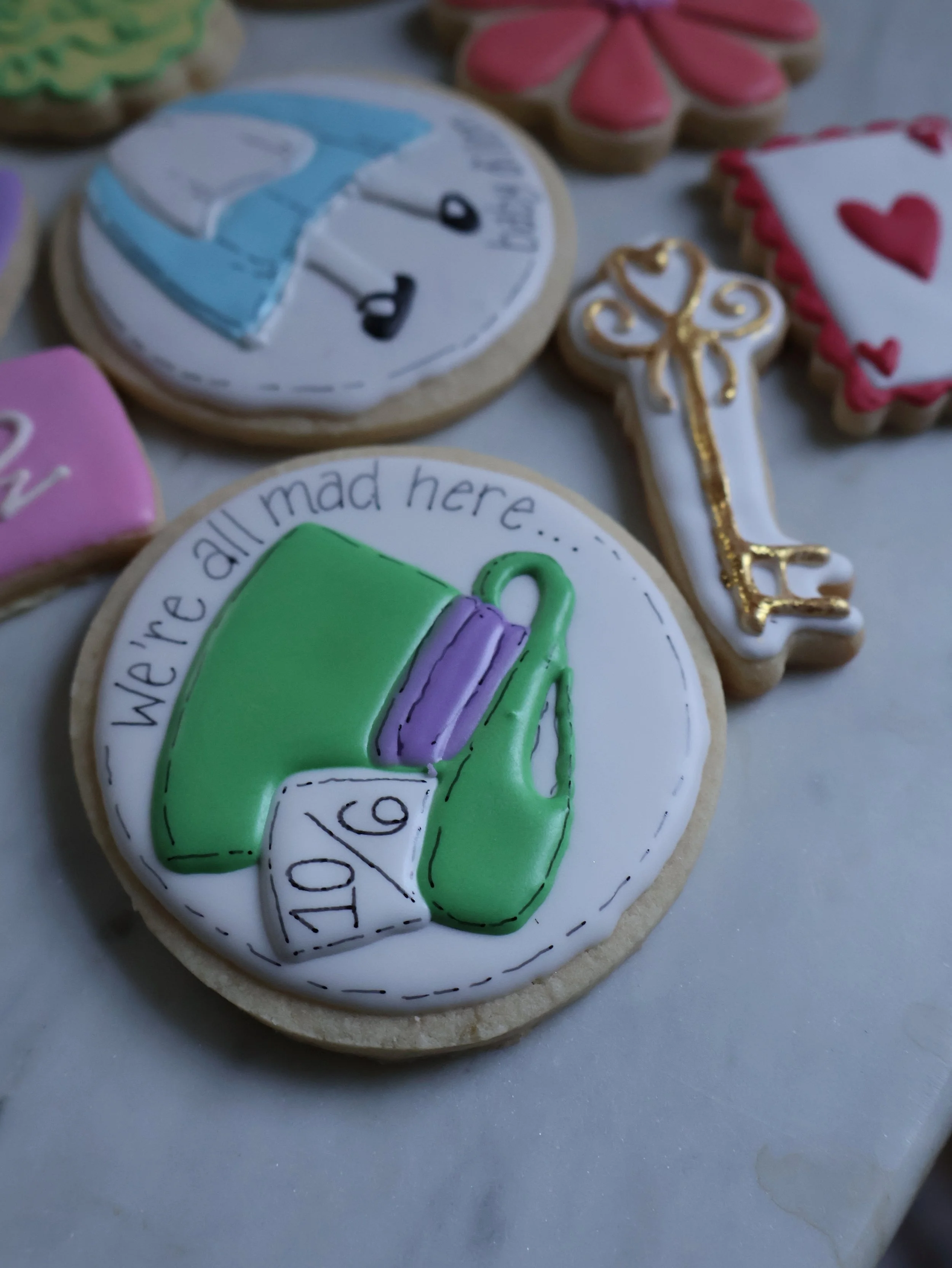 Decorated cookies with therapies' themes, including a green mug, purple thermometer, and the text 'We're all mad here...'