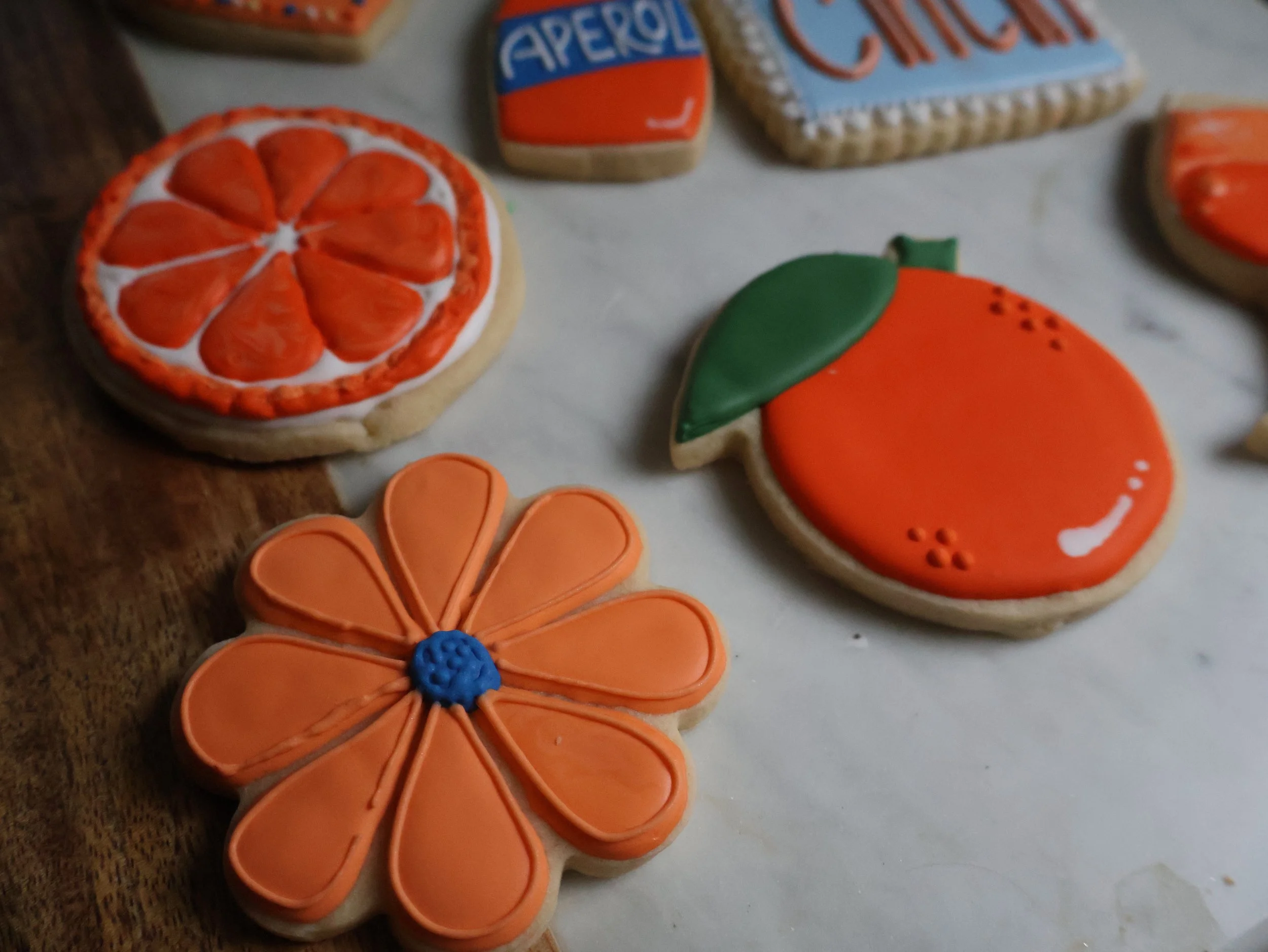 Decorated cookies shaped like a grapefruit, a flower, and a peach, laid on a white surface.