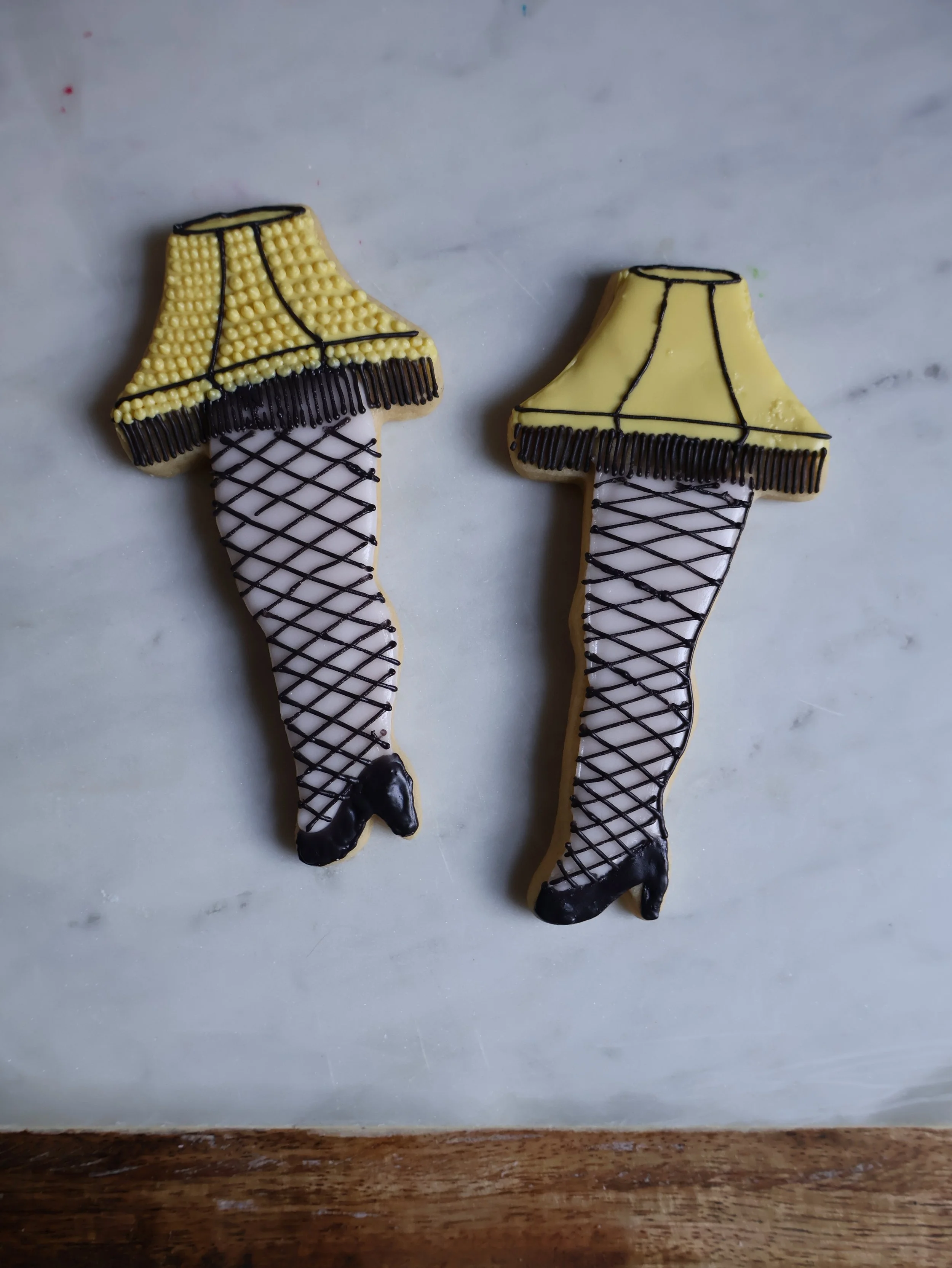 Decorated sugar cookies shaped like legs with fishnet stockings, black high heels, and yellow lamp shades as skirts.