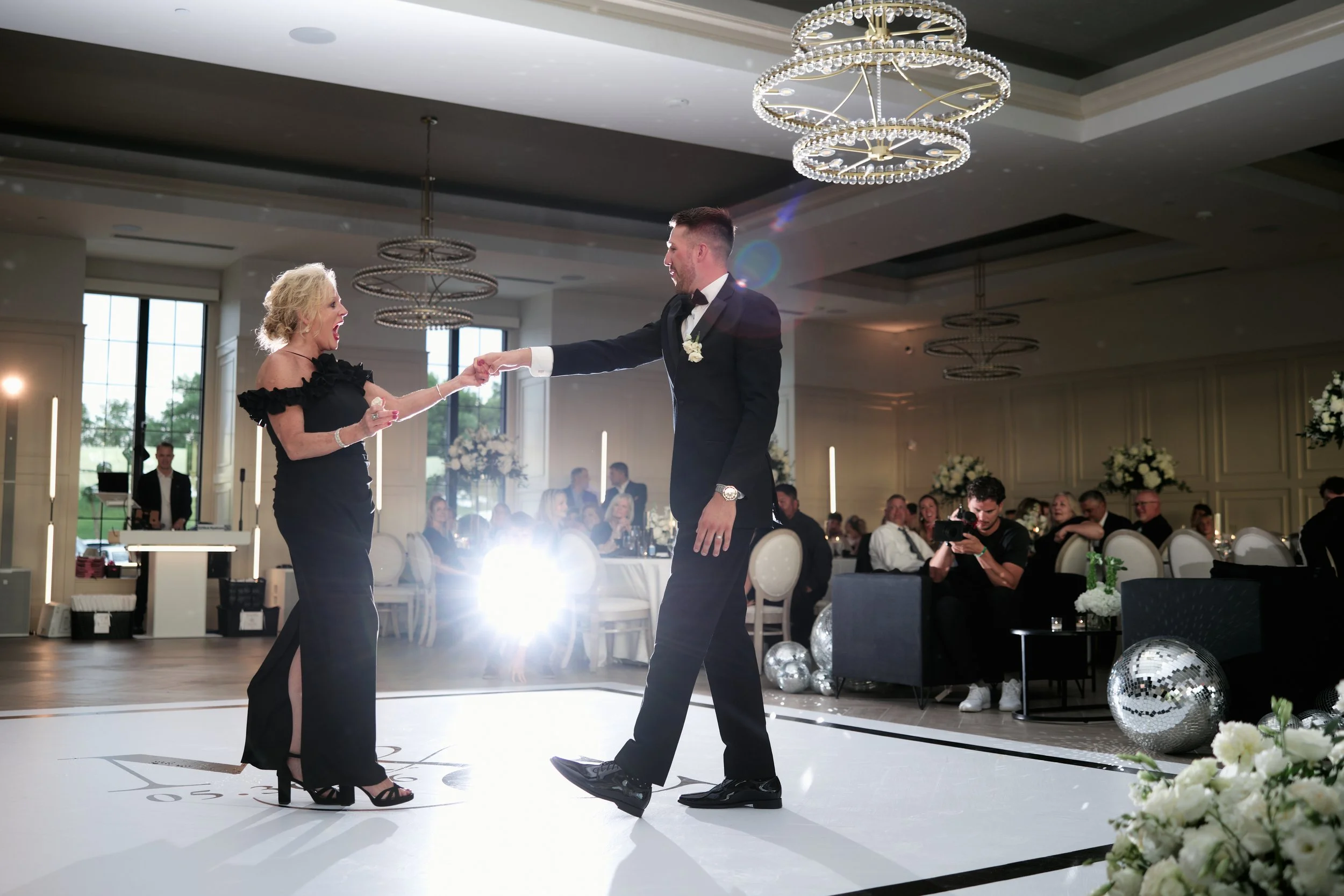 A couple dancing at a wedding reception in an elegant hall decorated with flowers and chandeliers.