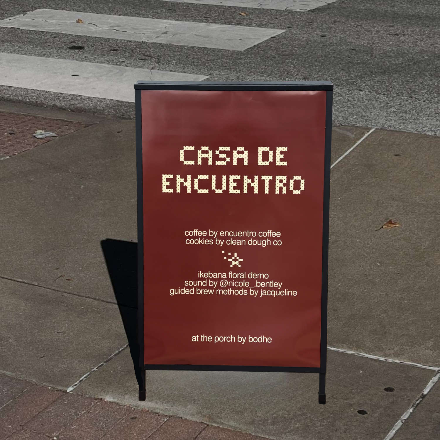 A sidewalk chalkboard sign with a maroon background displays white dotted text that reads 'CHAPAC ENCUENTRO.' Additional smaller white text below mentions coffee, cookies, a floral demonstration, sound, and brew methods, with some parts cut off at the bottom. The sign stands on a sidewalk with a street curb and a crosswalk visible in the background.