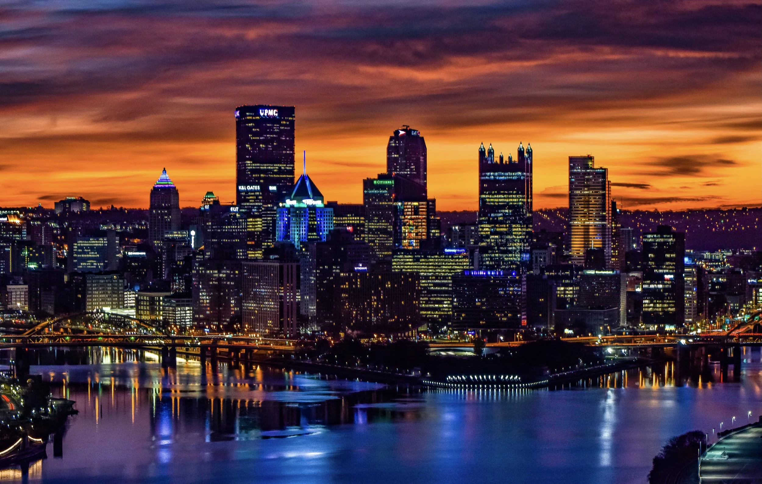 Pittsburgh skyline illuminated at night with city lights reflected on the river.