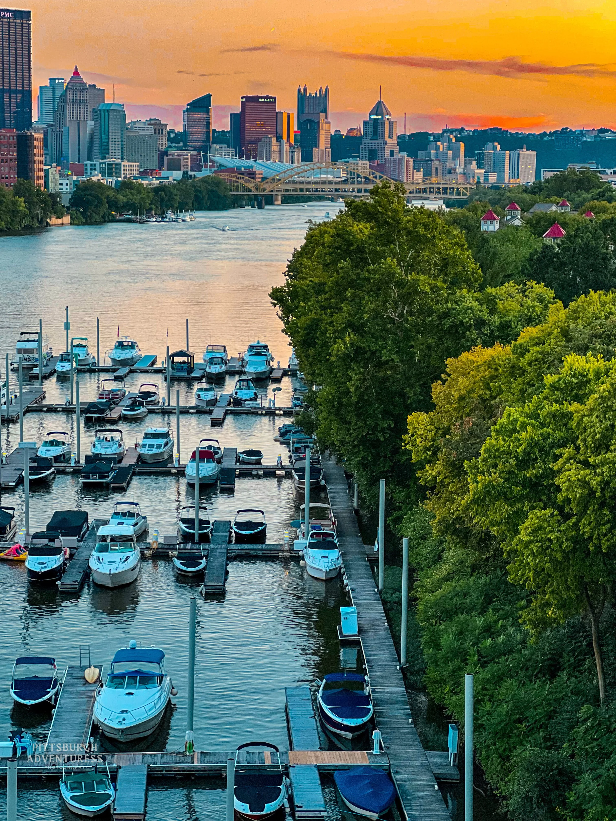 Herrs Island. Pittsburgh skyline seen from riverfront marina with boats and tree-lined shoreline.