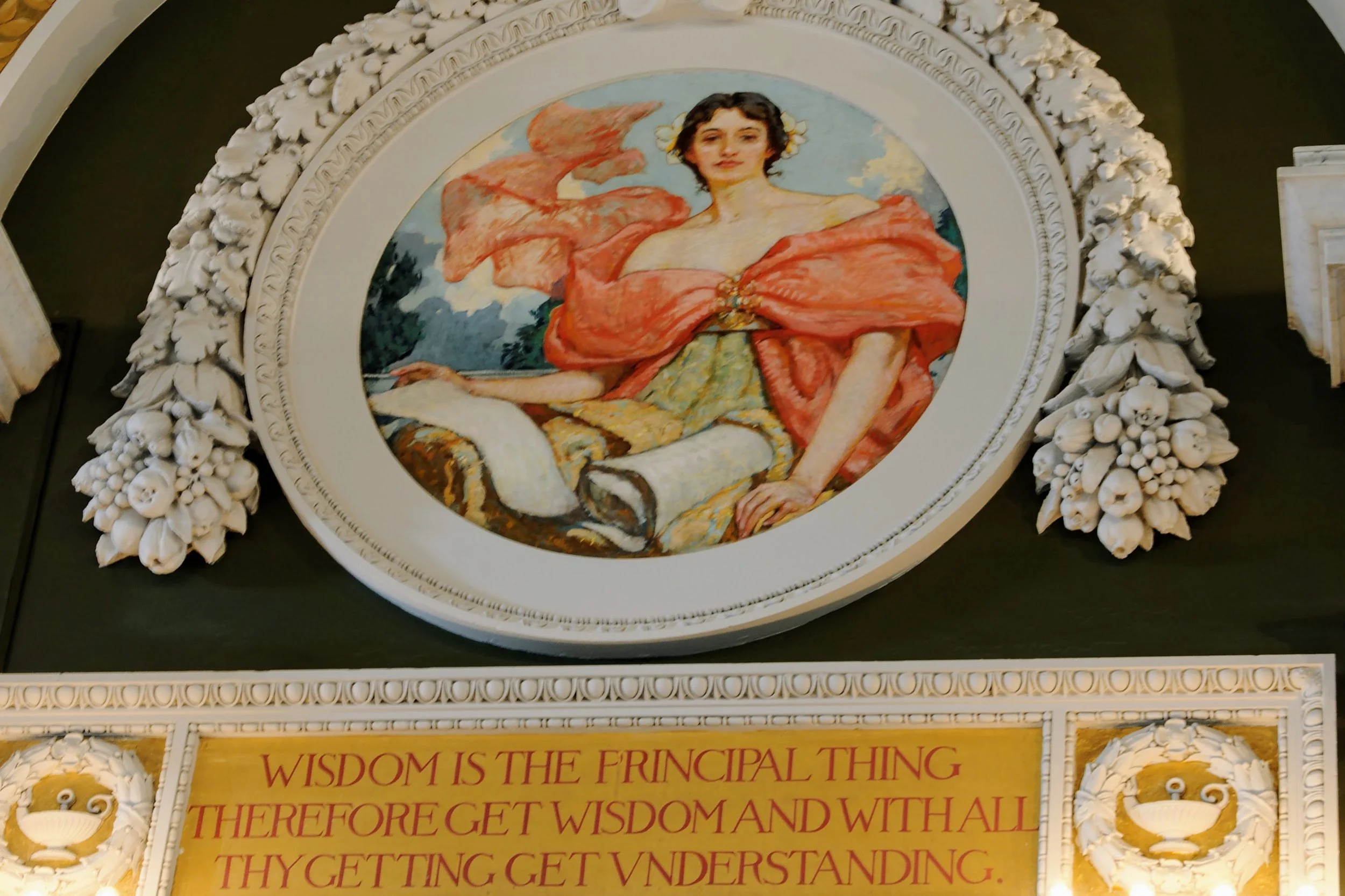 A decorative framed painting of a woman with dark hair in a colorful dress, sitting outdoors with a landscape background. The frame has floral and fruit motifs. Below the painting, there's a quote on a yellow background that reads: "Wisdom is the principal thing therefore get wisdom and with all thy getting get understanding."