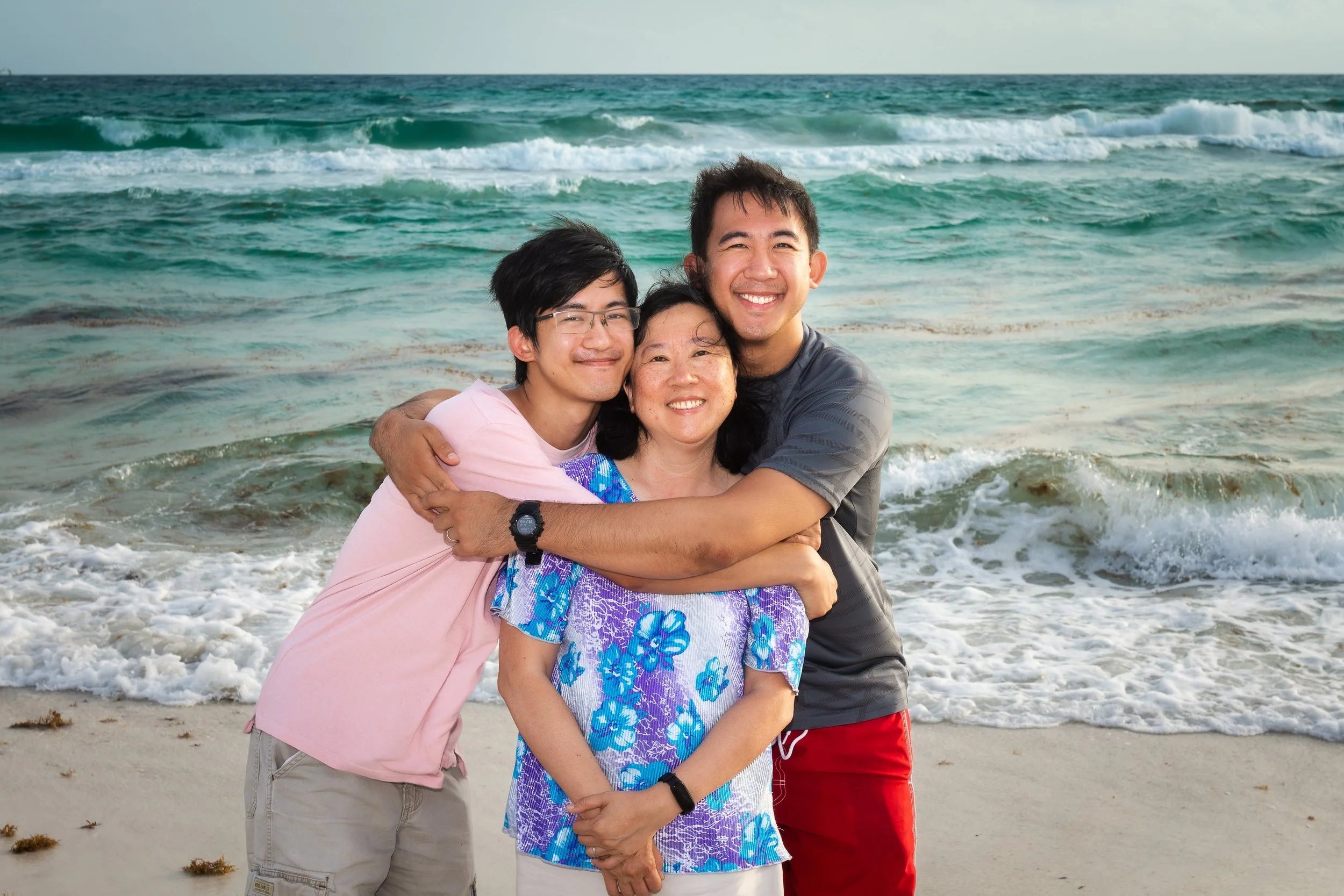 Three people hugging by the ocean on the beach, smiling.