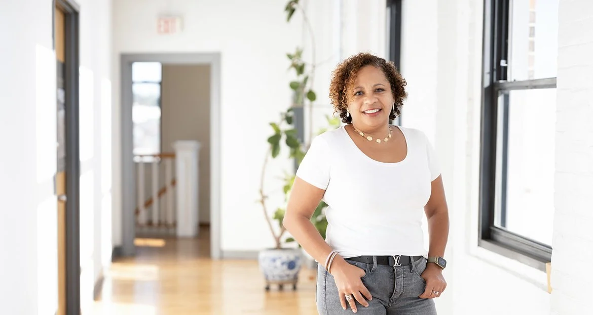 Smiling woman standing in bright room with large windows and potted plant