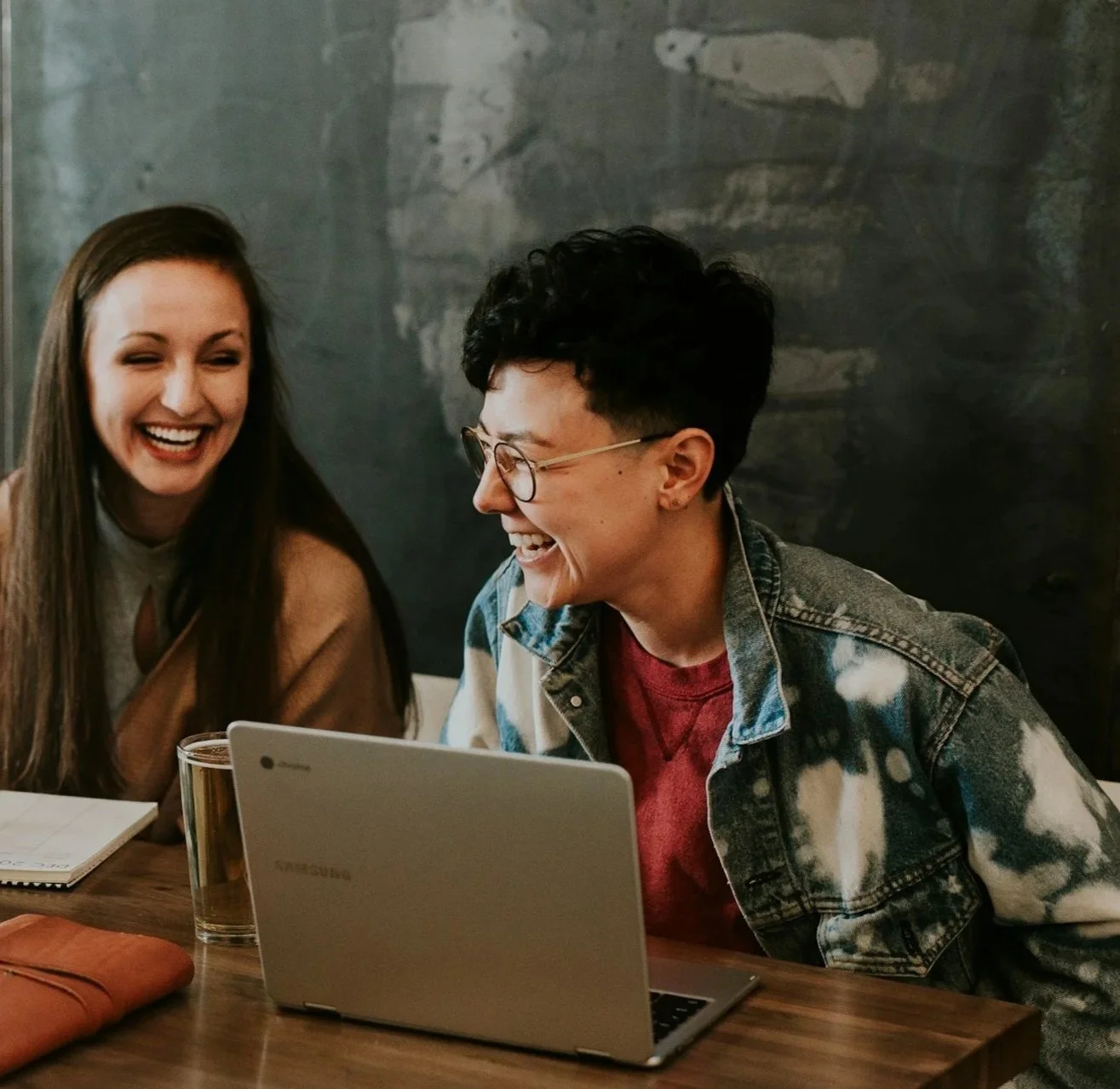 man and women laughing at a cafe with laptops in front of them