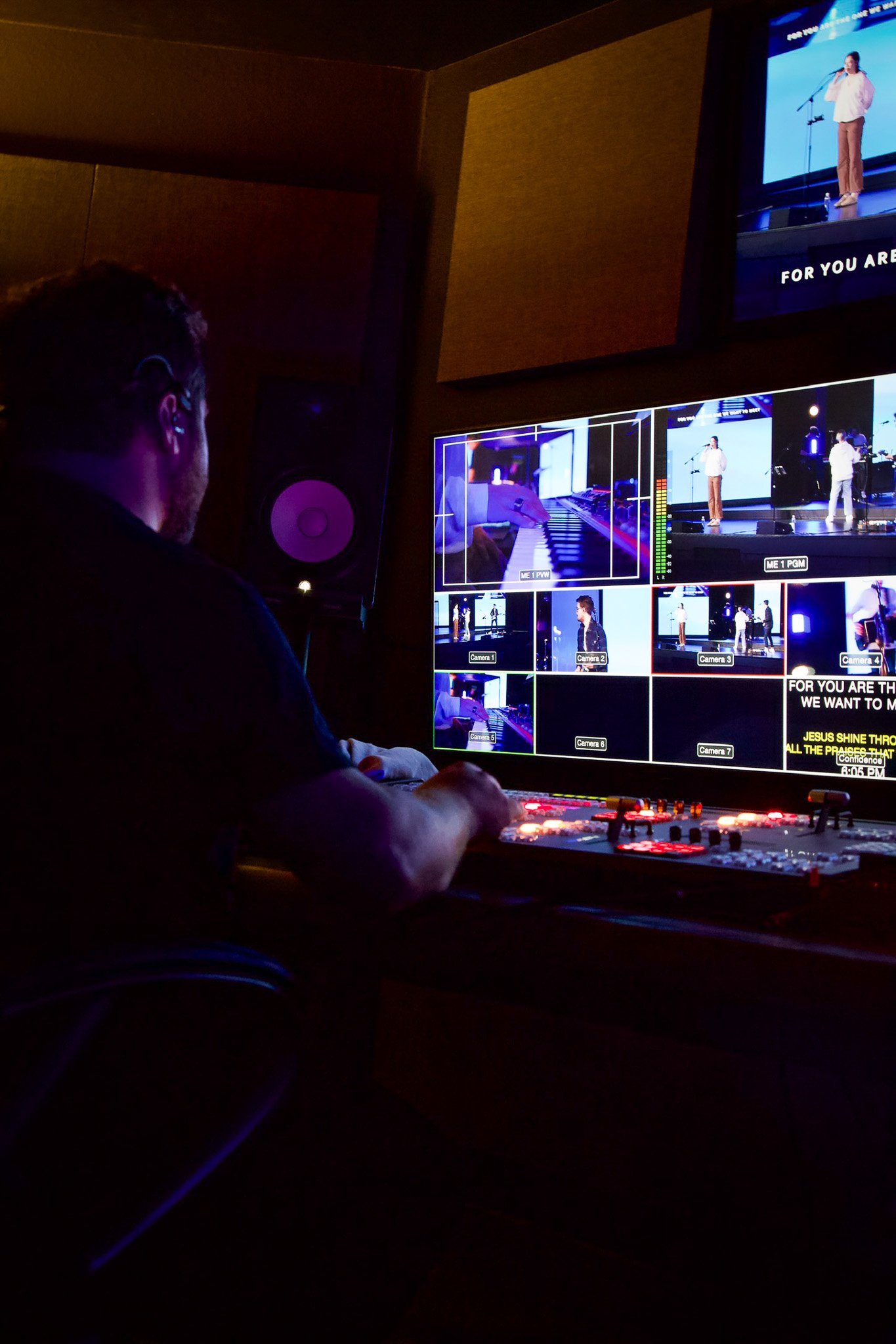 A person working in a control room with multiple monitors showing a stage performance and camera feeds.