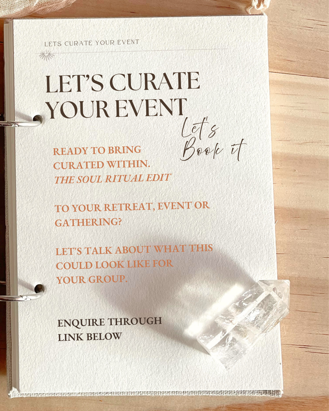 Invitation or brochure with textured cream-colored paper, promoting event curation and booking. The text includes phrases like 'Let's Curate Your Event,' 'Ready to bring curated within,' 'The Soul Ritual Edit,' and mentions enquirers to use a link below. There are two clear quartz crystals placed at the bottom right corner of the paper, resting on a wooden surface.