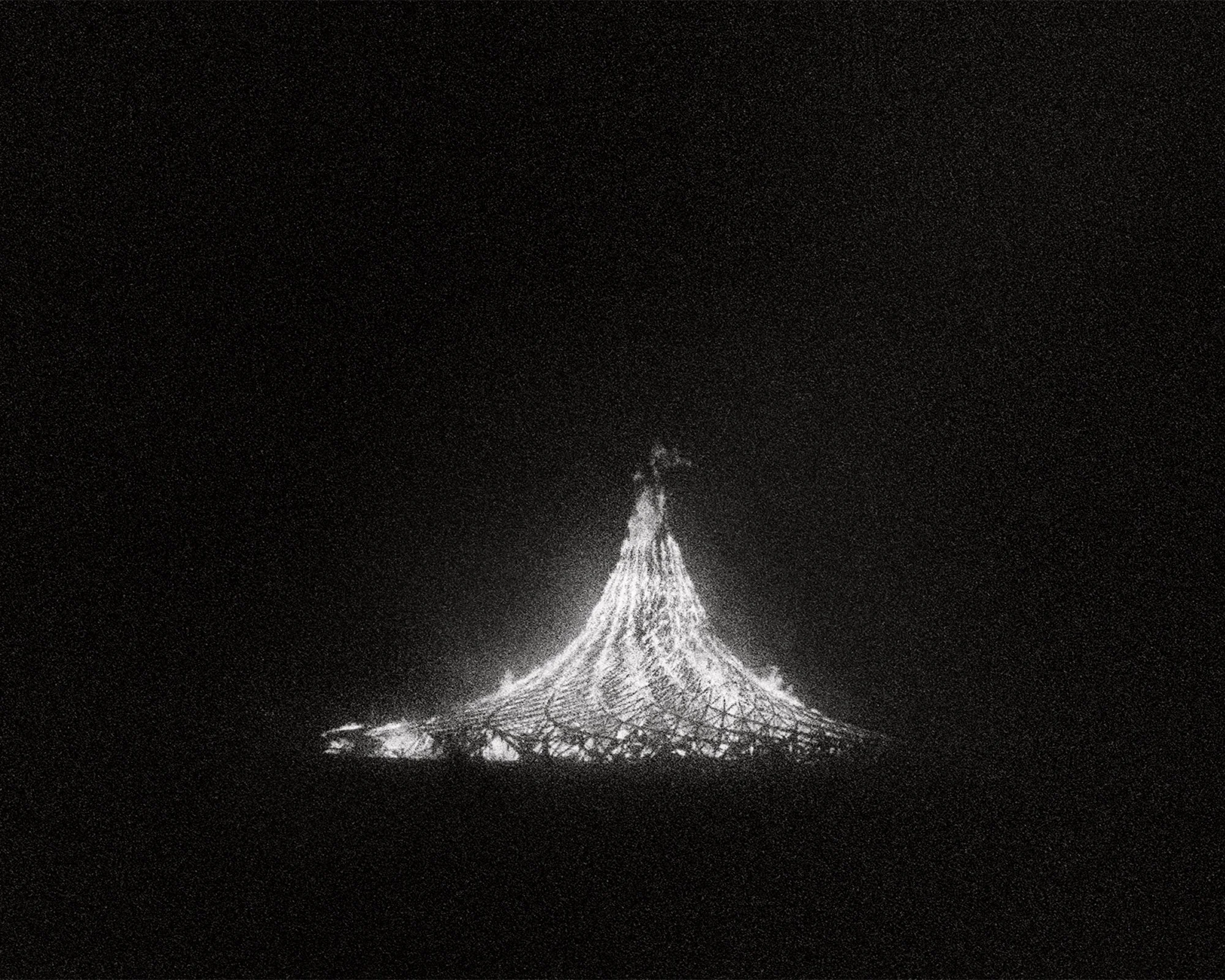 Illuminated sculpture resembling a mountain or volcano at night, with a glowing, lattice-like structure.