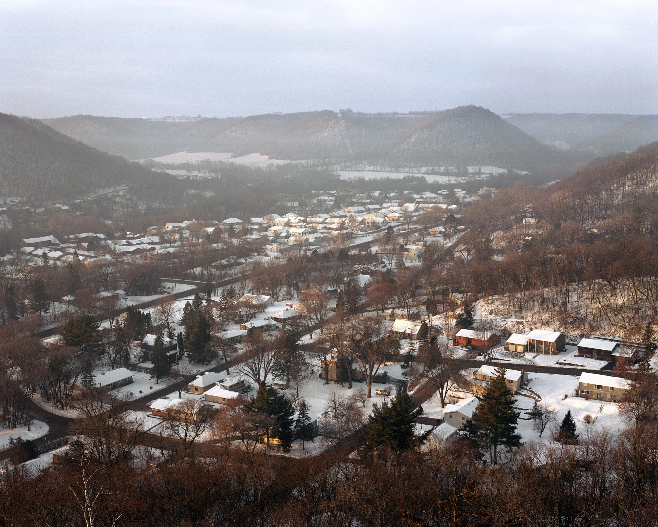 Aerial view of a snow-covered residential neighborhood in a valley surrounded by hills and mountains.