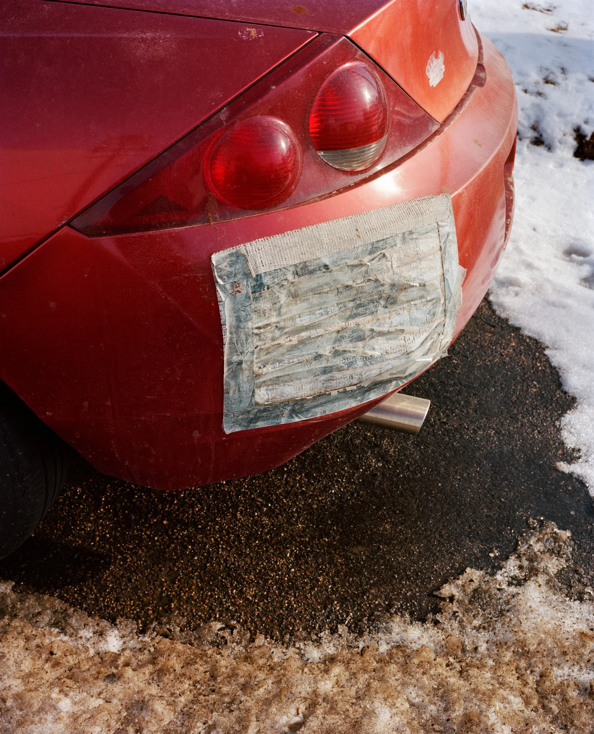 Red sports car with taped rear license plate area, parked on snowy and wet asphalt.