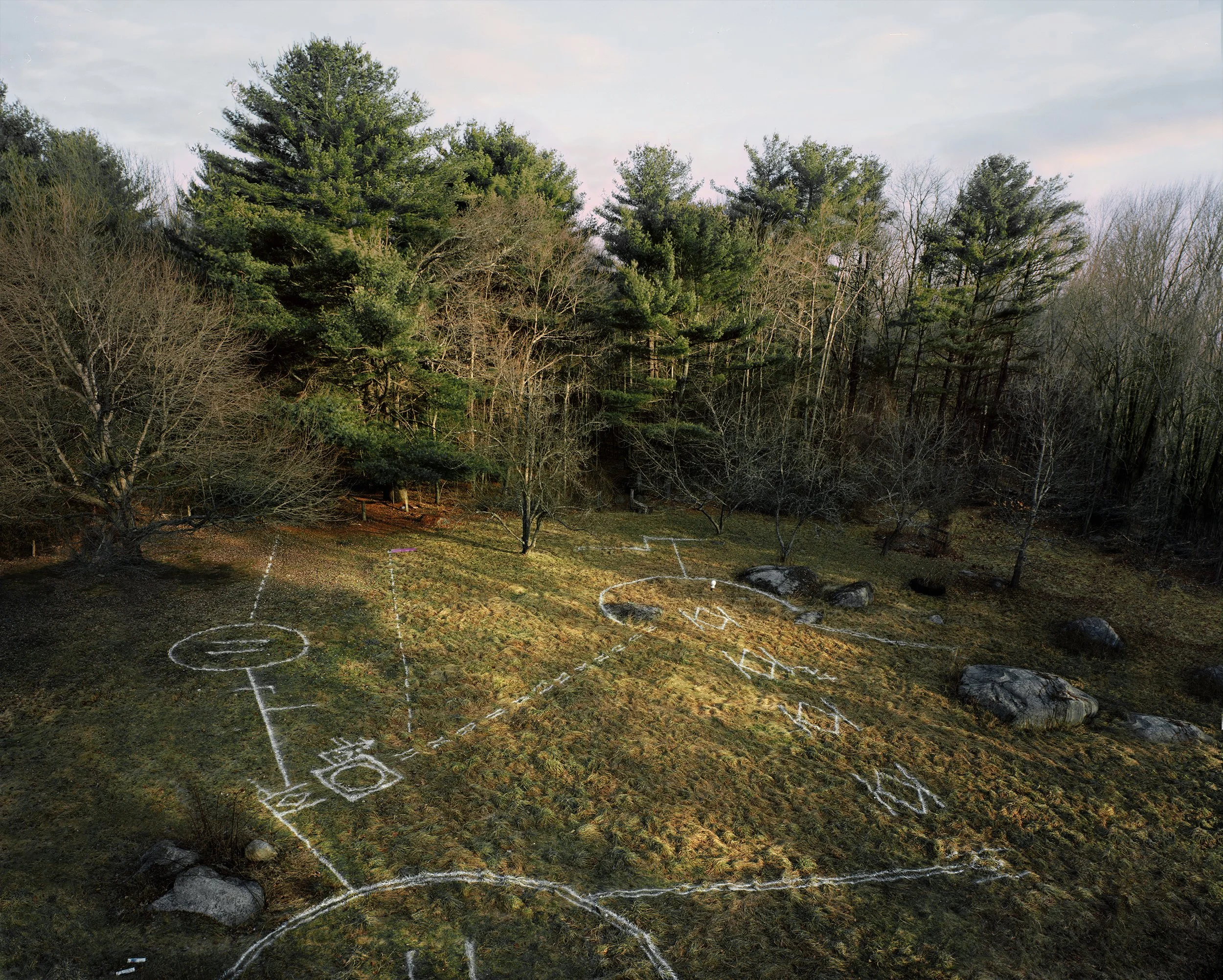 Bird's eye view of a backyard with a homemade hopscotch and game outline chalked on the grass, surrounded by trees and rocks.