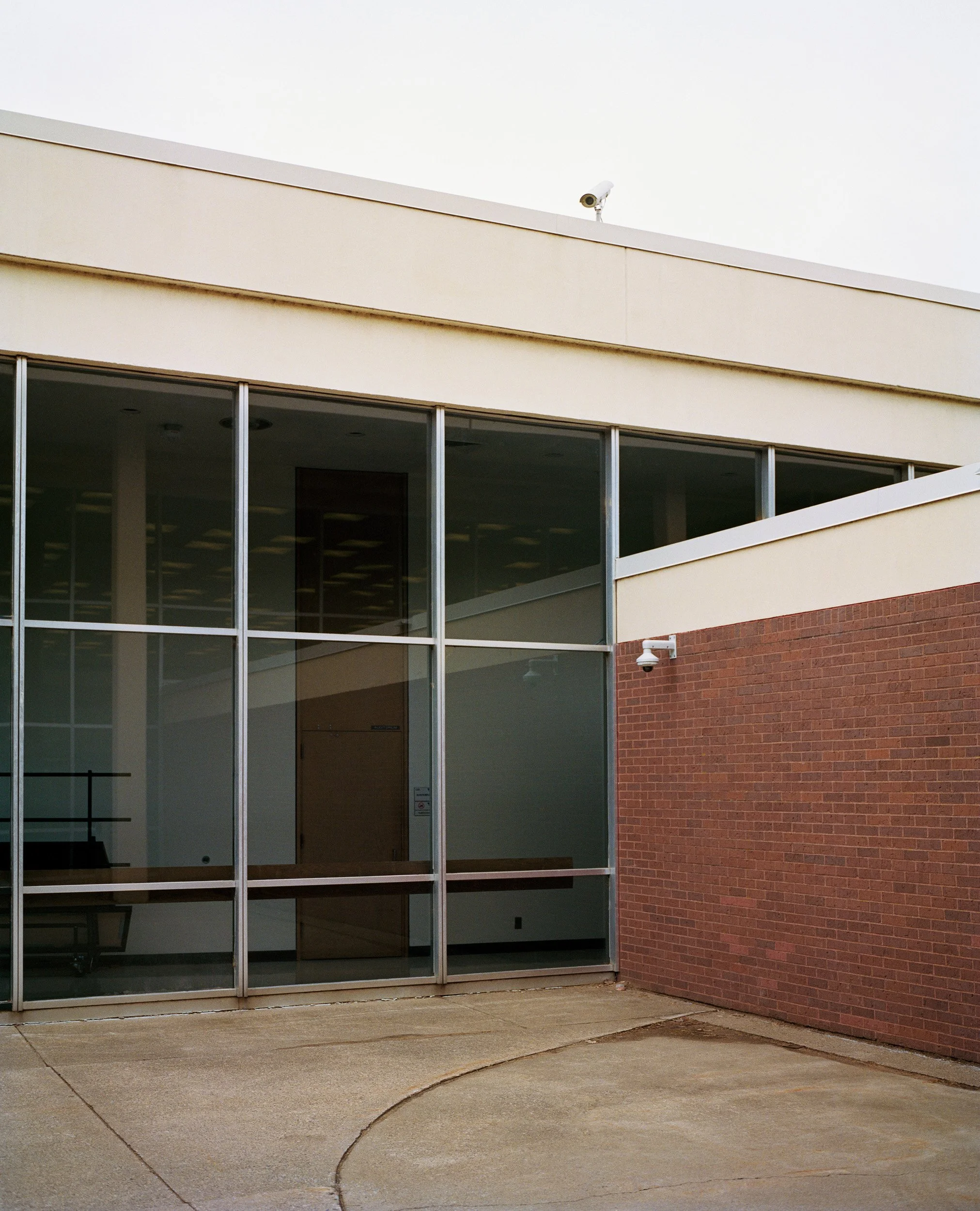 Modern building exterior with large glass windows, a part of a brick wall, and security cameras on the roof and wall.