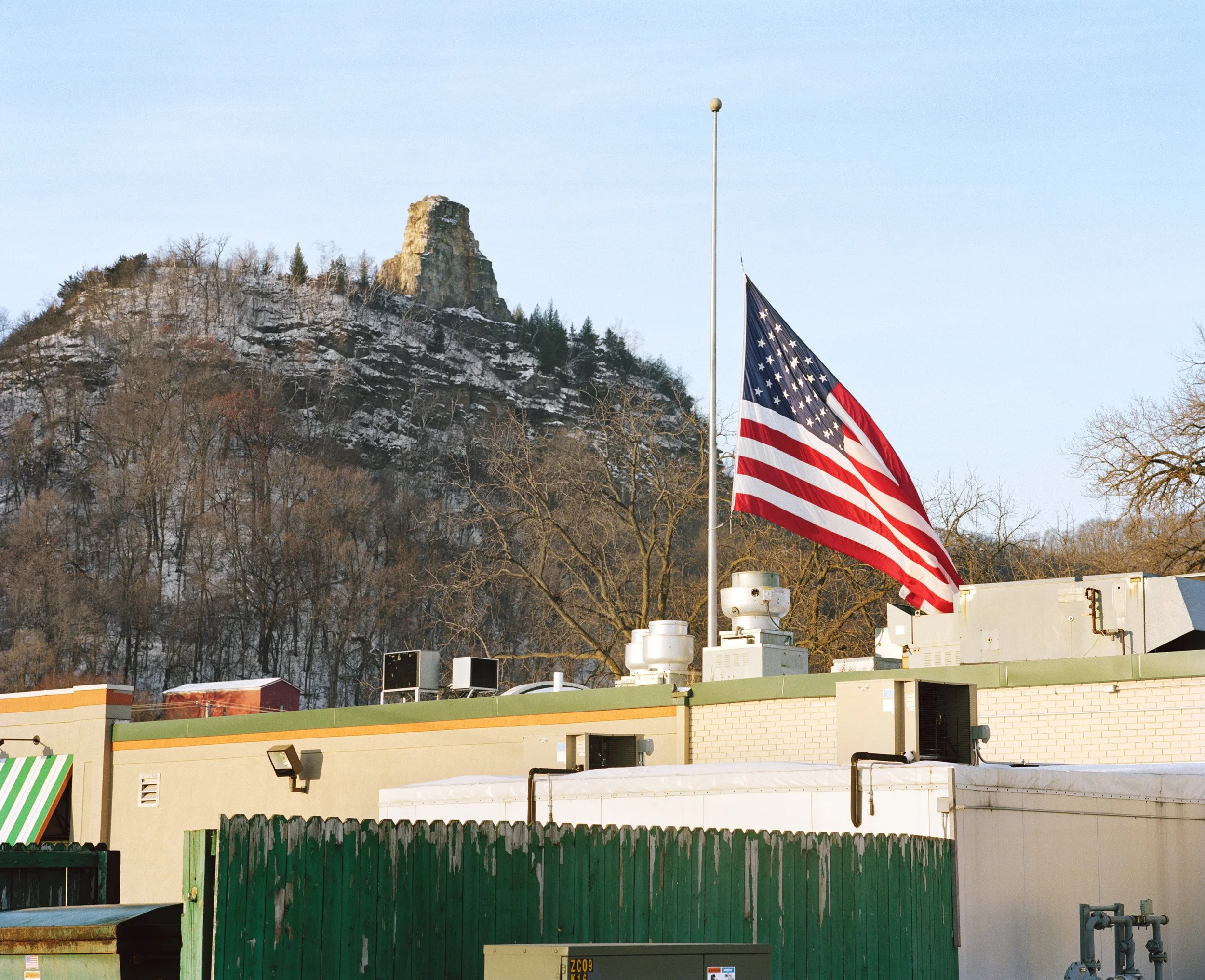 American flag flying on a pole above rooftops with a snow-covered mountain in the background.
