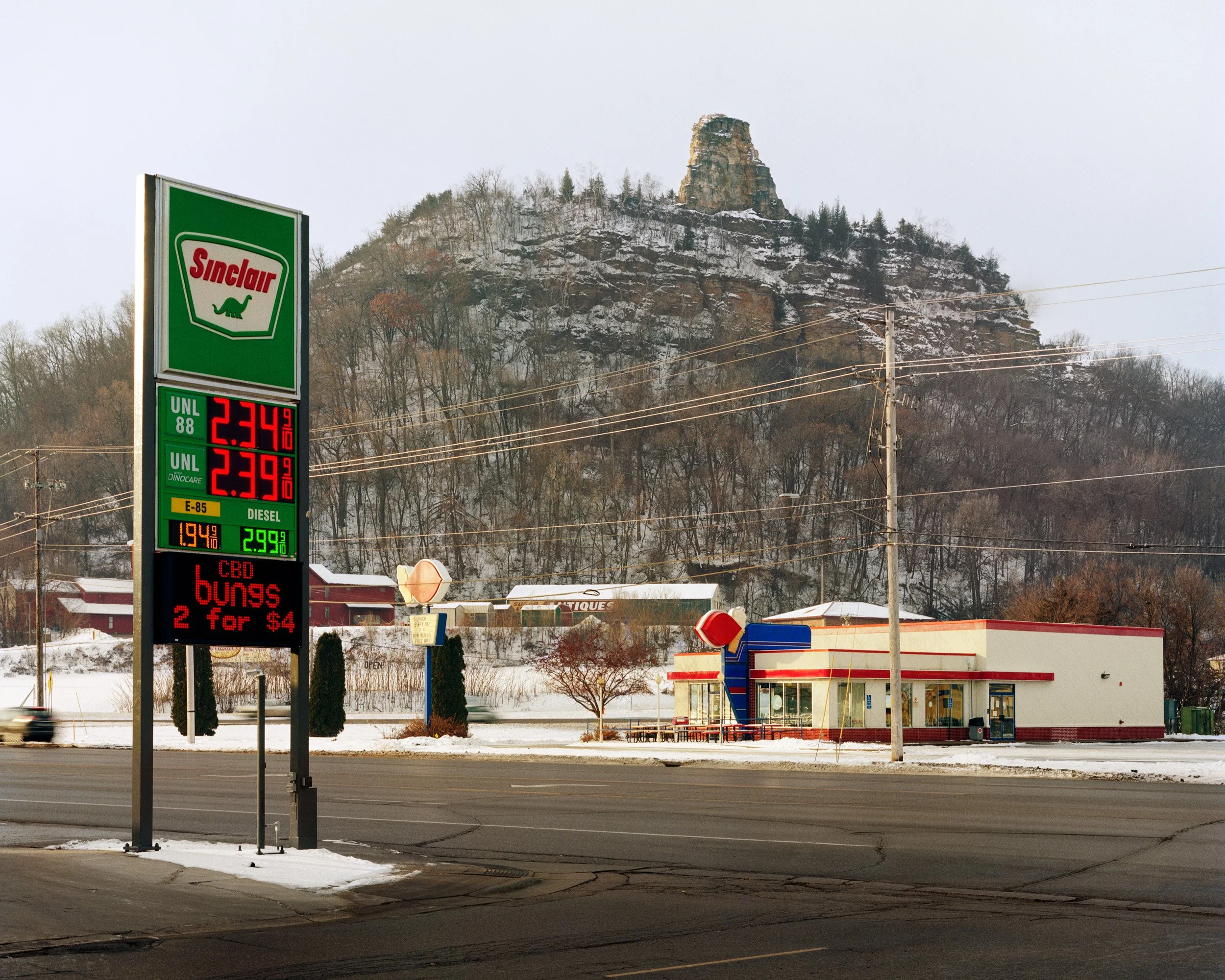 Sinclair gas station with a mountain in the background, snow on the ground, and fuel prices displayed on the sign.