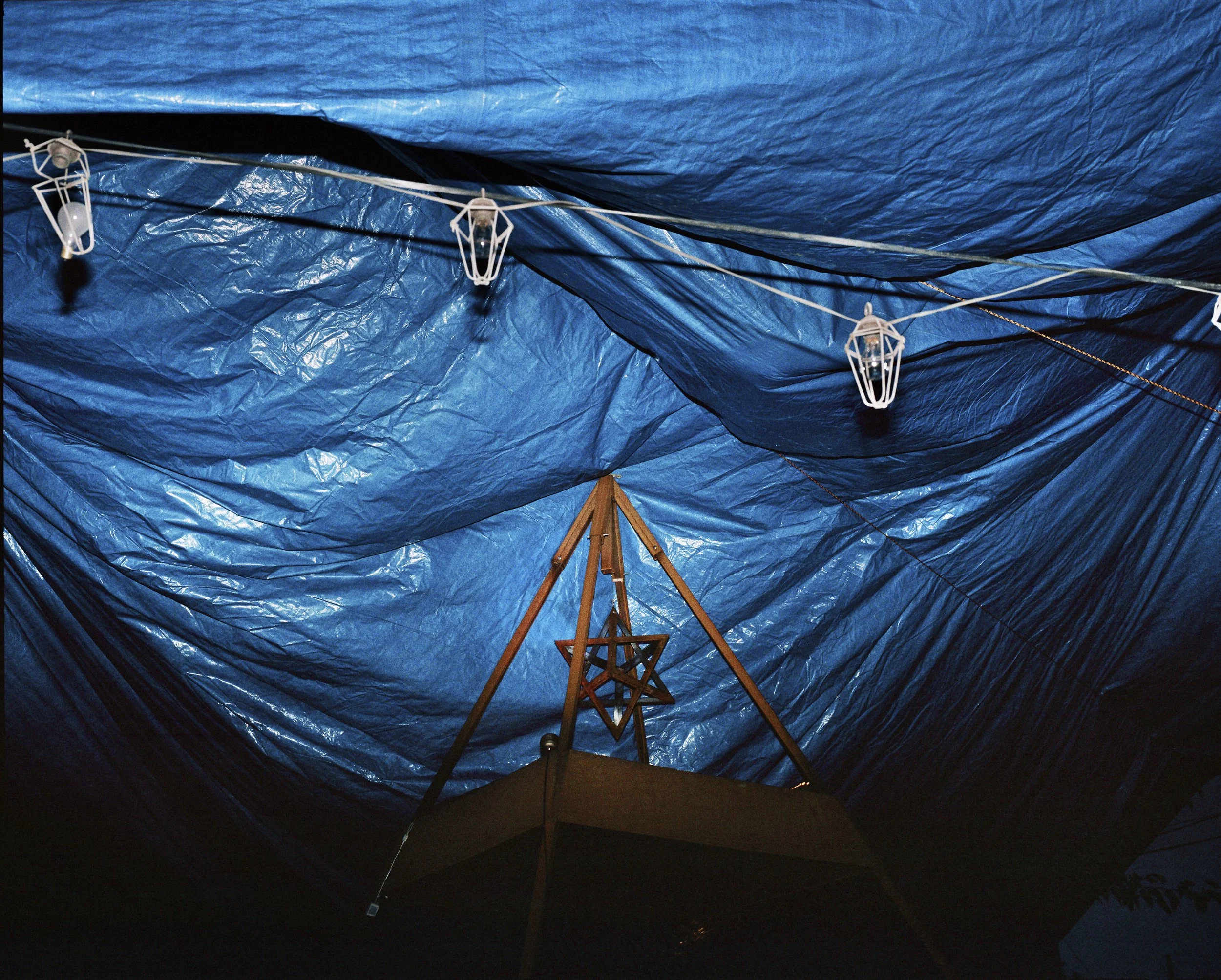 Blue tarp ceiling with string lights and a wooden star-shaped ornament hanging from a pole.