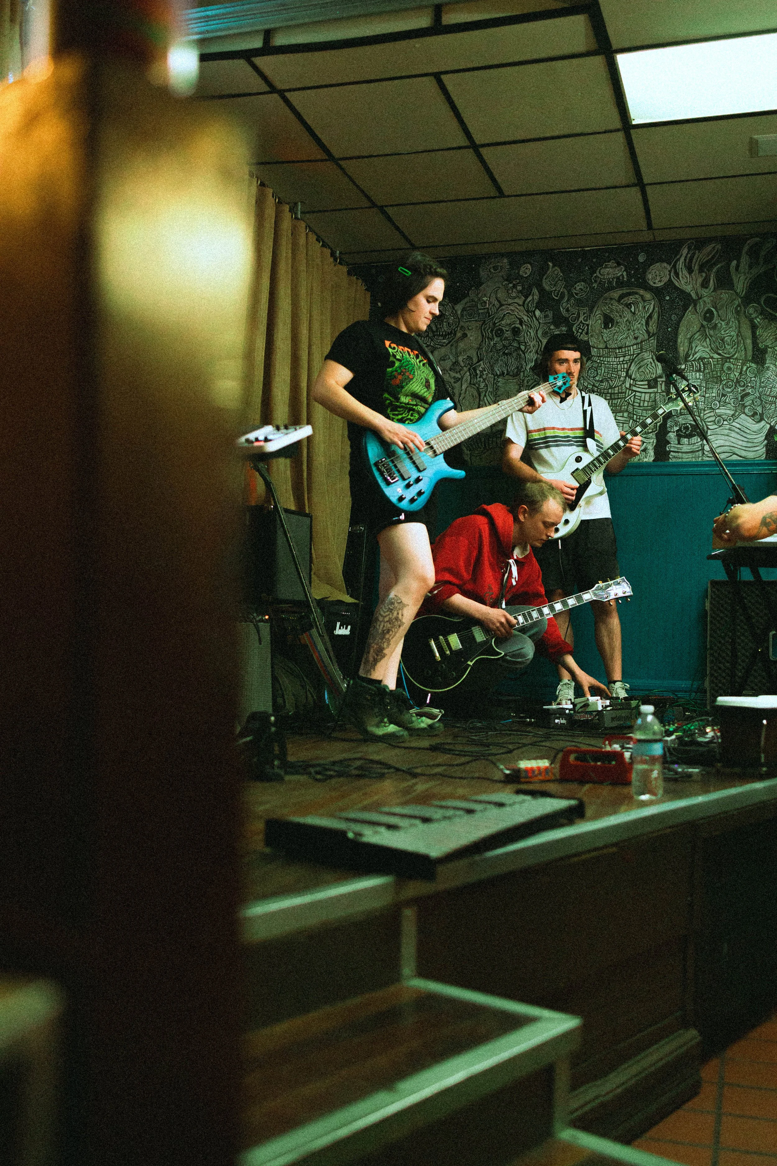 People playing musical instruments during a live performance in a dimly lit room with graffiti art on the wall.