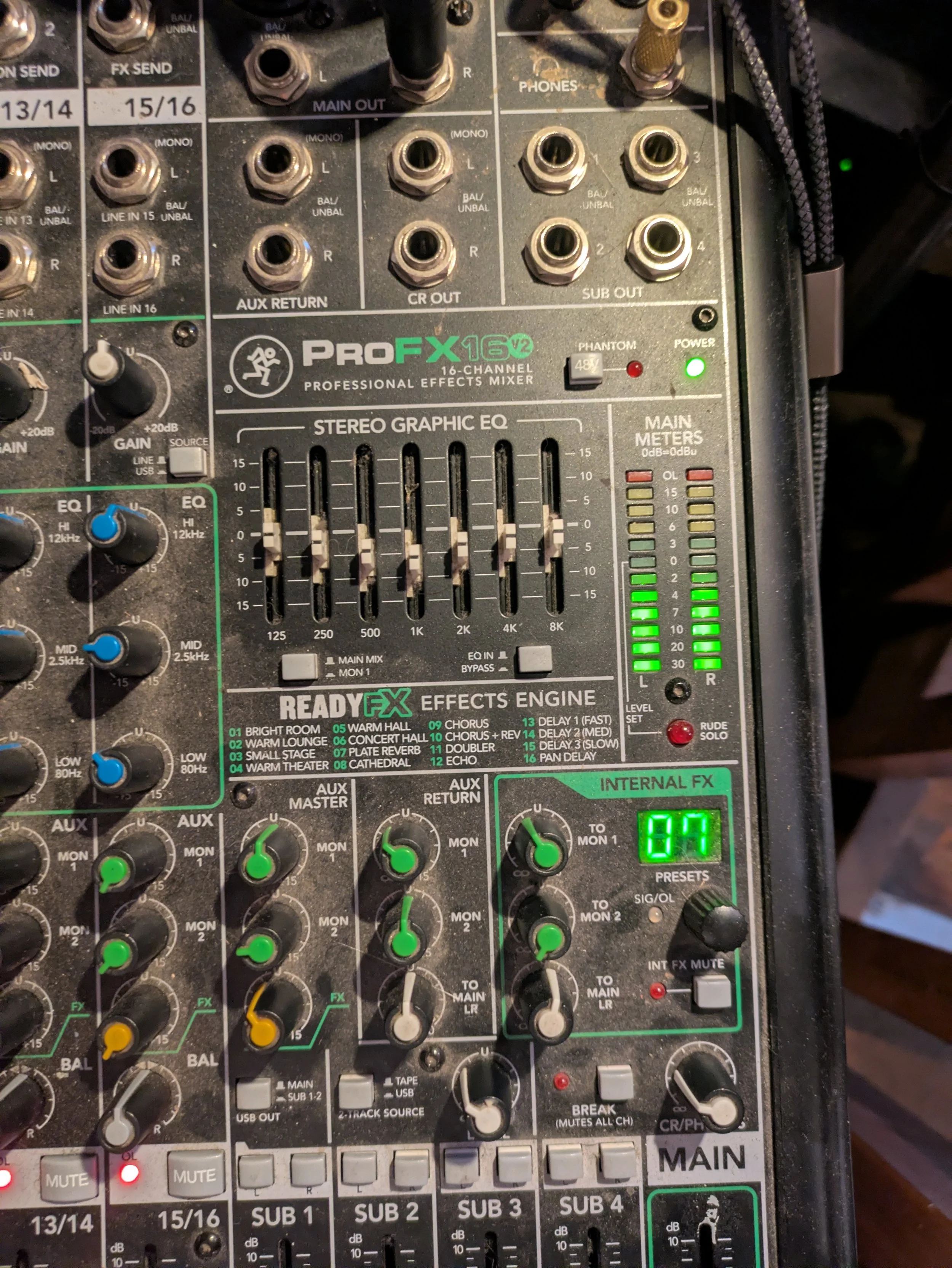 Close-up of a professional audio mixing console with various knobs, sliders, and connectors, including input/output ports, equalizer controls, and meters.