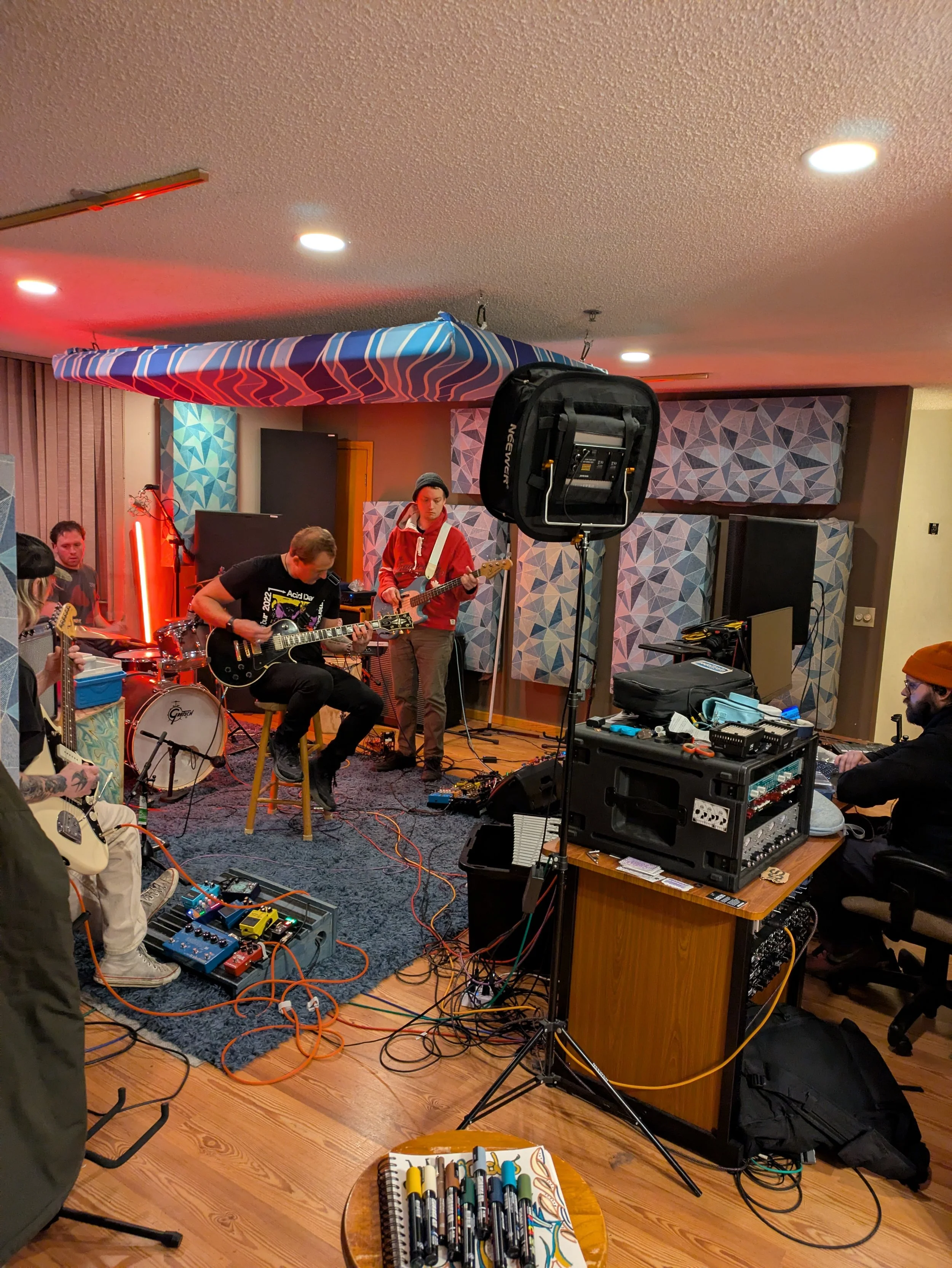 Band practicing in a recording studio with musical instruments, audio equipment, and colorful soundproofing panels.