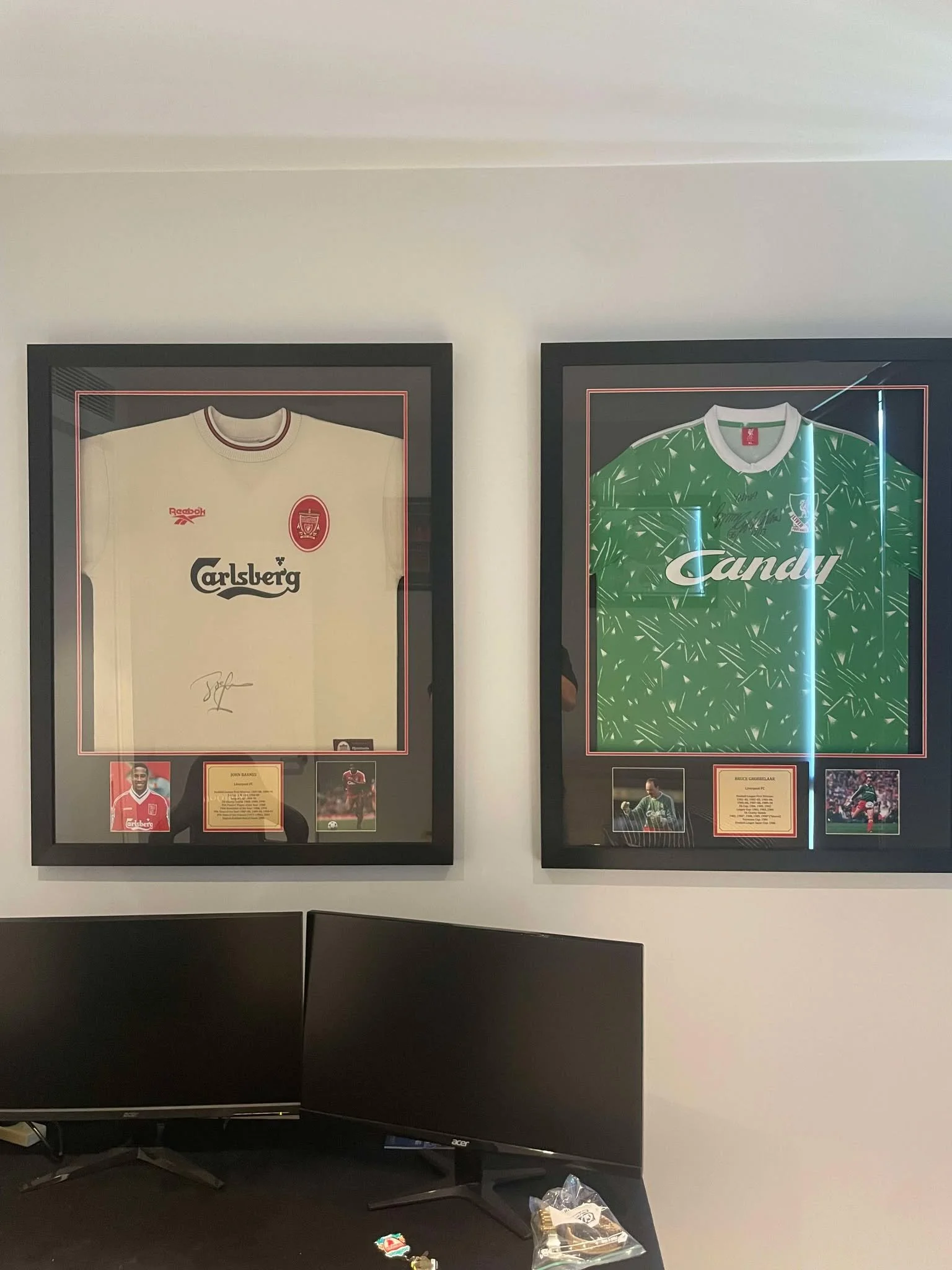 Two framed sports jerseys hanging on a wall, with small photos and plaques beneath each. The left jersey is white with red accents, and the right jersey is green with white accents.