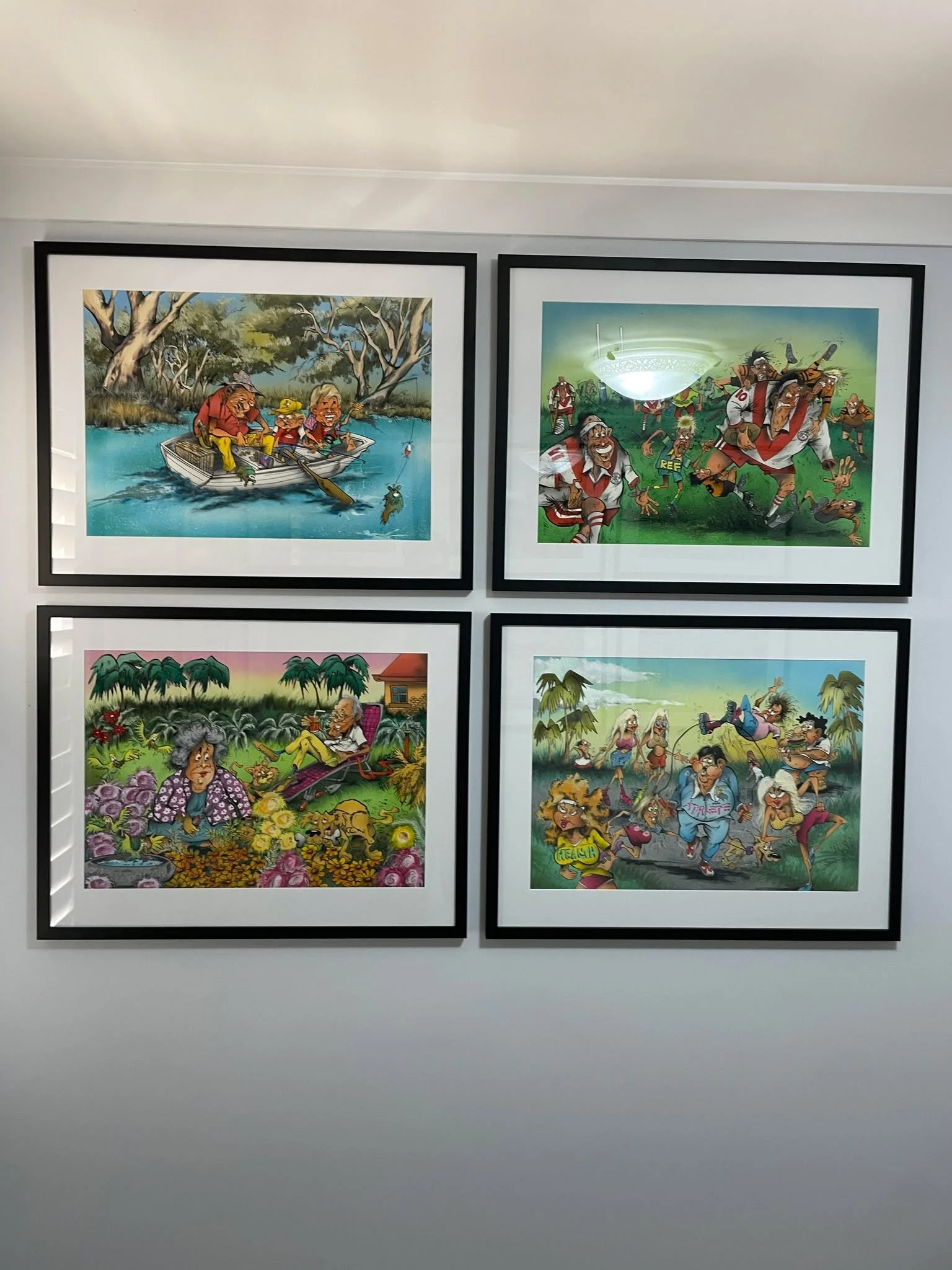 Four framed cartoon illustrations hanging on a wall, depicting humorous scenes with exaggerated characters in various outdoor settings.