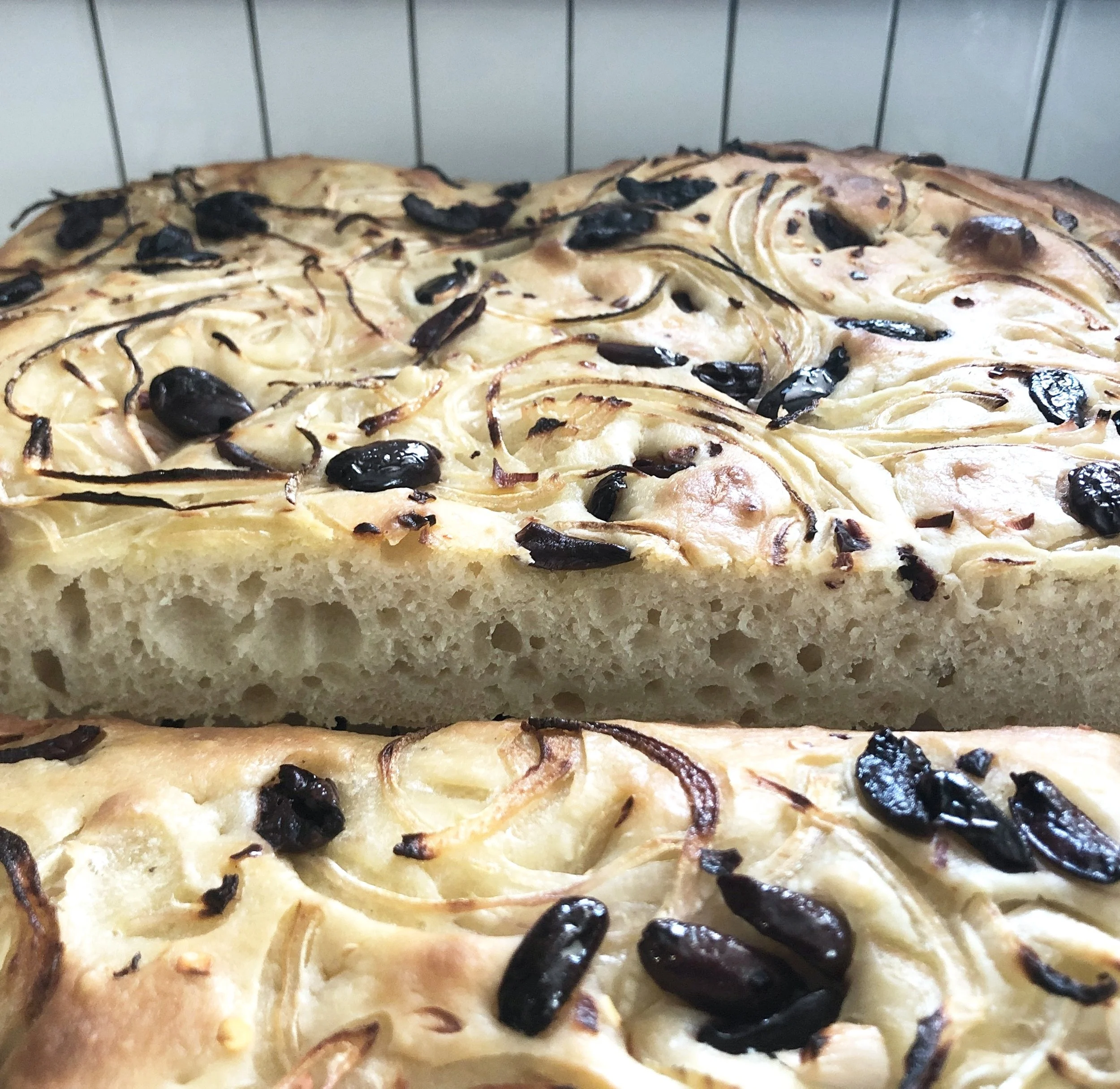 Close-up of a baked focaccia bread topped with dried chiles, black olives, and onion slices.