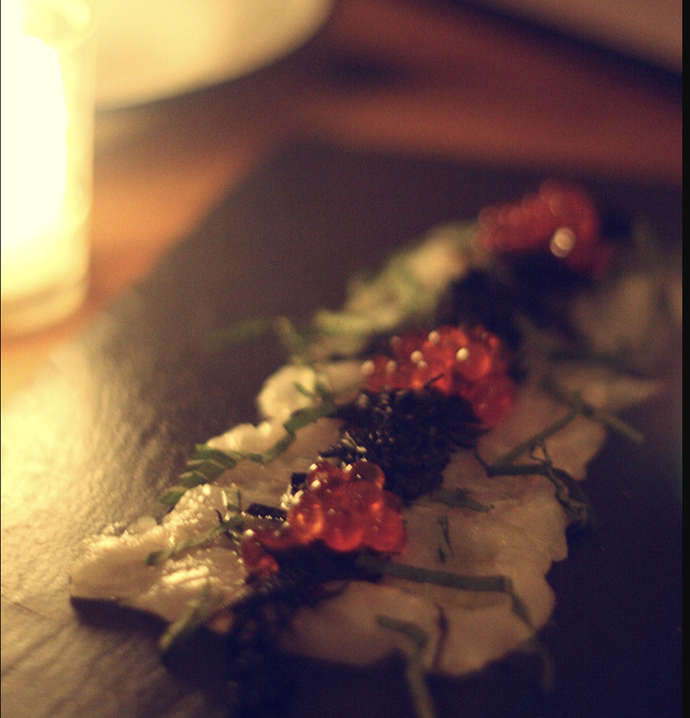 Close-up of a festive appetizer with red caviar and greens on a white base, lit by warm candlelight.