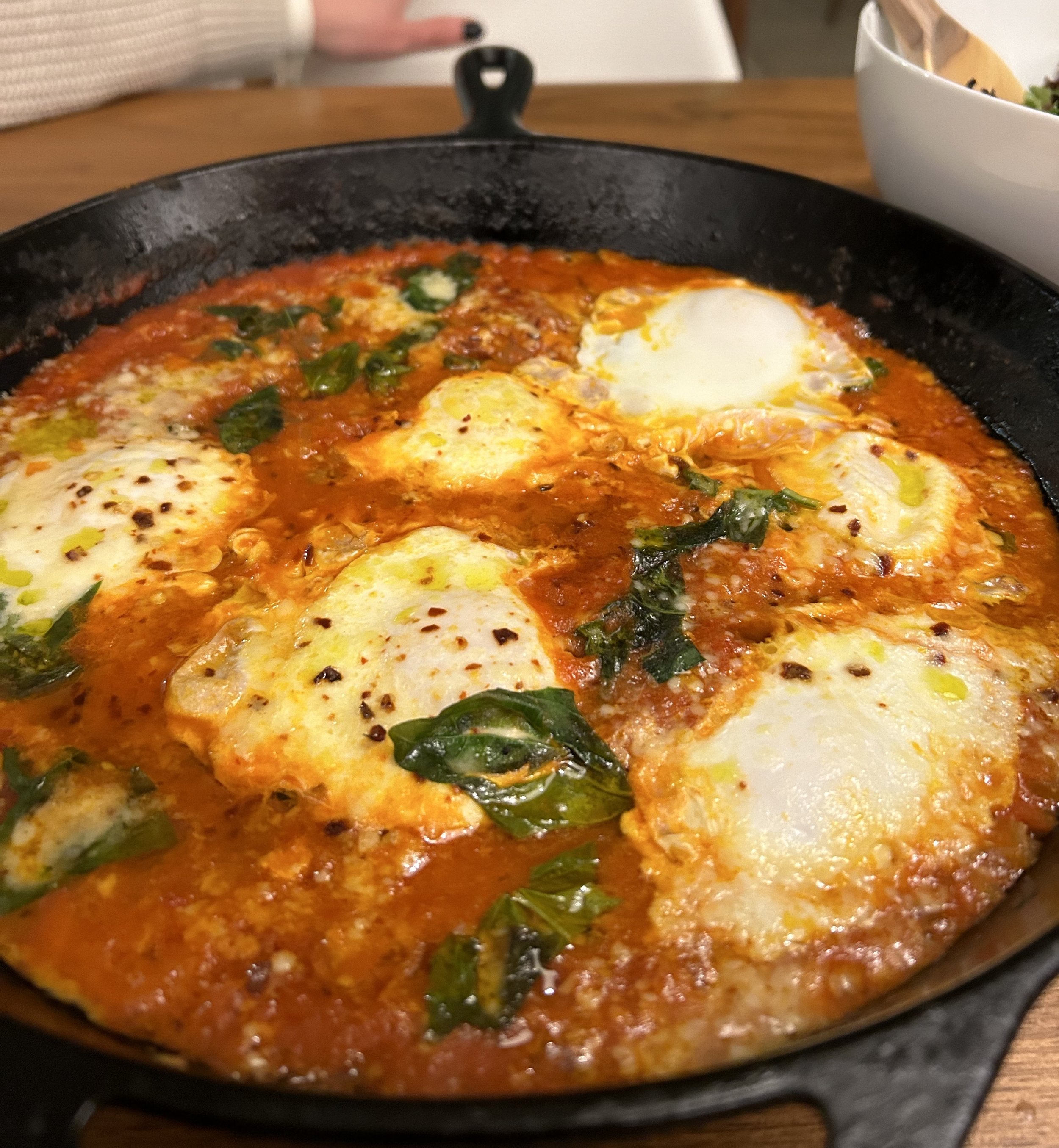 Skillet of eggs in tomato sauce with basil leaves.