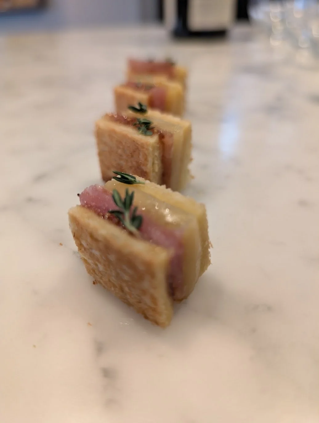 Close-up of small, layered sandwich squares garnished with herbs on a white surface.