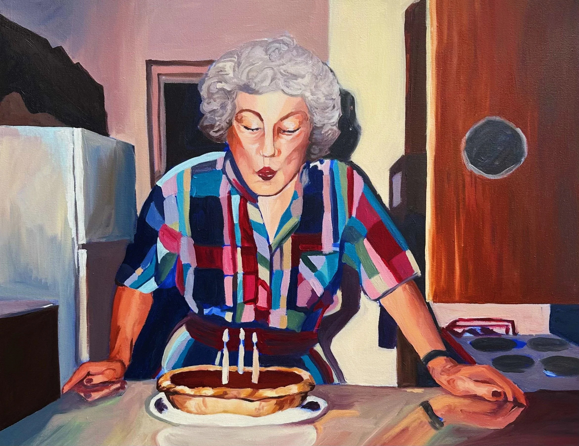 A woman with curly gray hair wearing a colorful striped shirt, sitting at a table with a pie in front of her, inside a room with warm-colored walls.