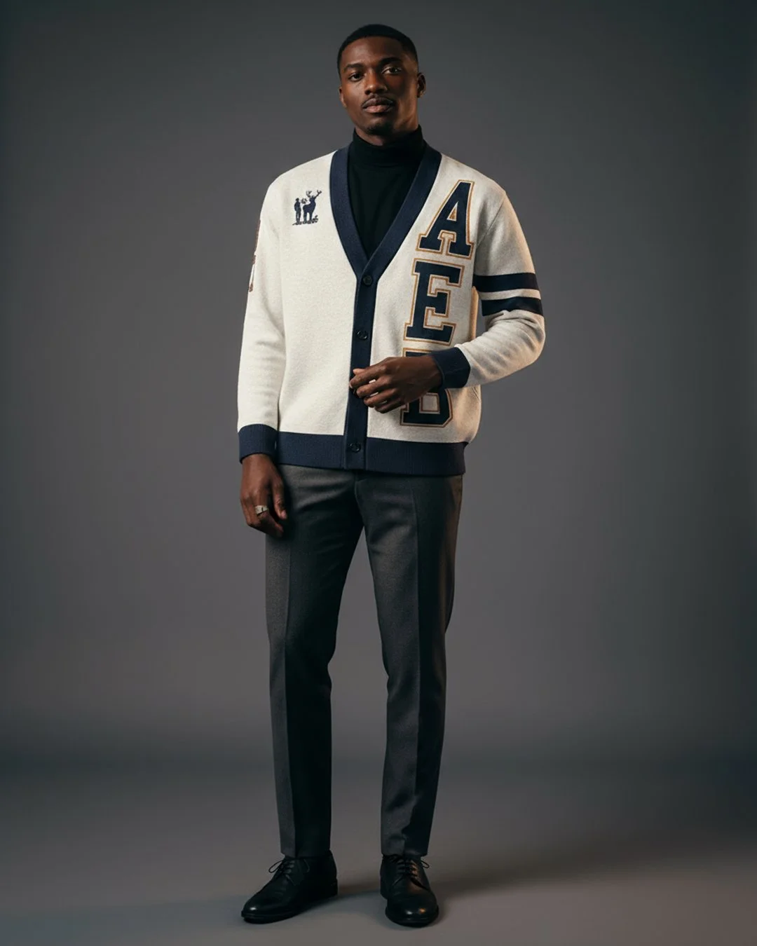 Full-body Black male model in varsity cardigan with bold AEB lettering, layered over black mock-neck, slim dark trousers, leather Chelsea boots, minimal accessories, cinematic soft light, neutral grey seamless studio background, editorial fashion look.jpg