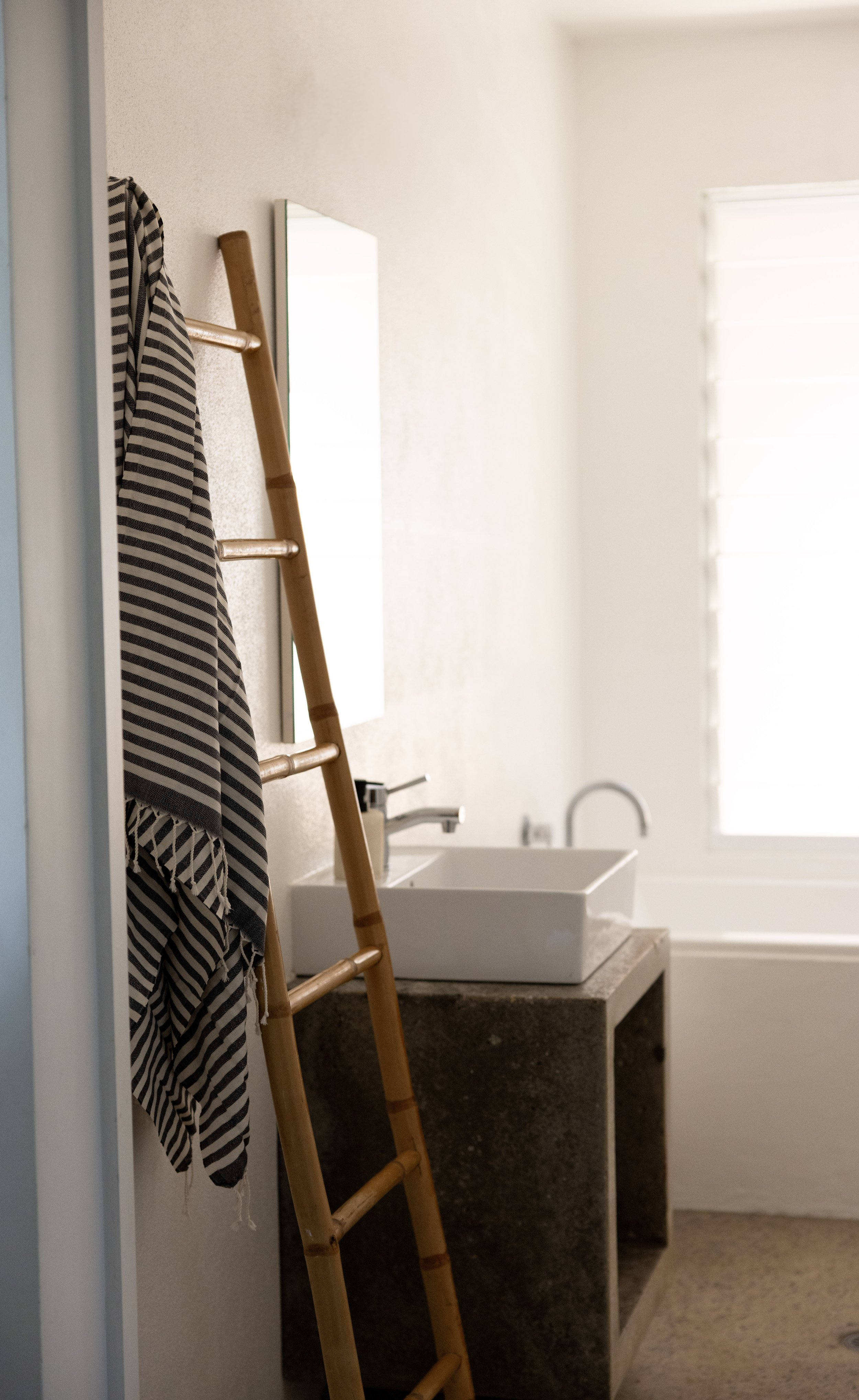 Minimalist bathroom with wooden ladder towel rack and polished concrete details at Haven Tropicana.