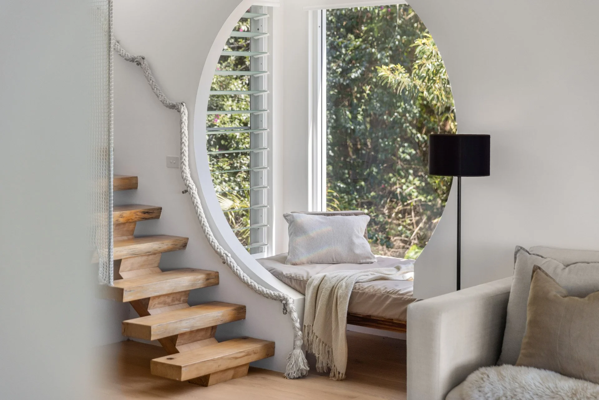 A peaceful reading nook framed by a striking circular window overlooking tropical gardens.