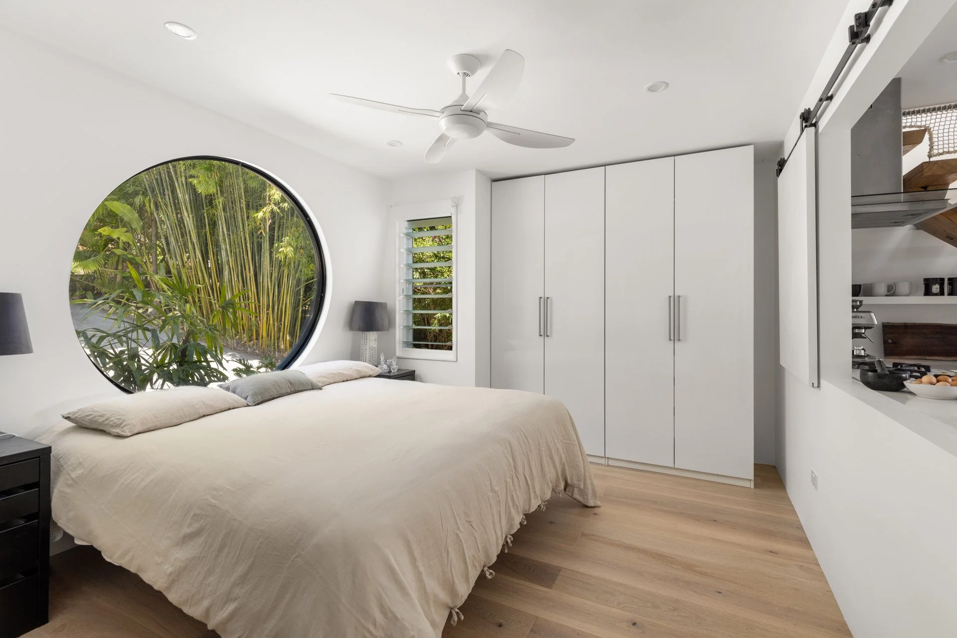 A peaceful king bedroom with a striking circular window overlooking lush tropical gardens.