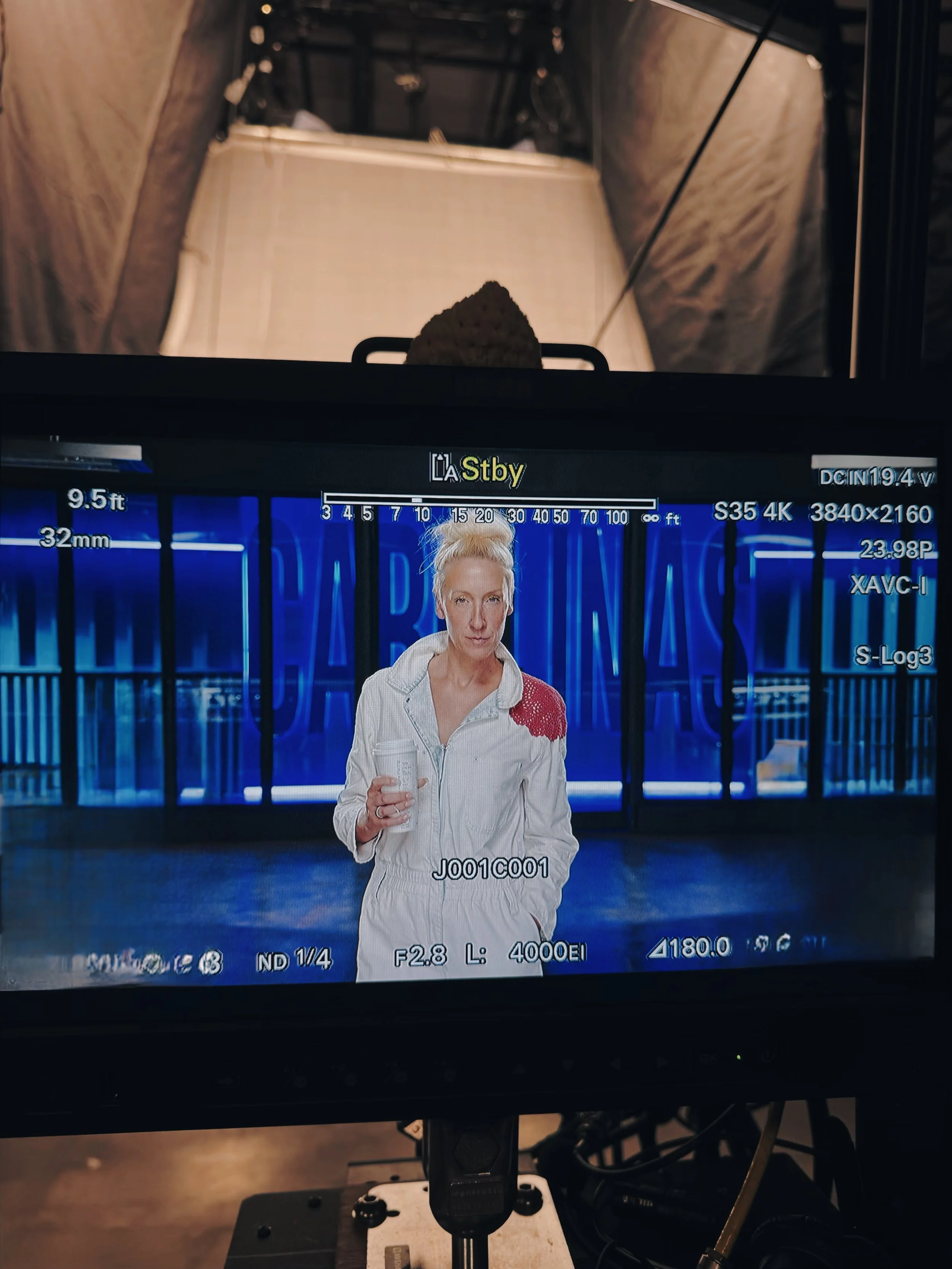Anna Moulaison behind the camera capturing a woman with blonde hair in a white jacket holding a glass in front of a neon-lit blue background.
