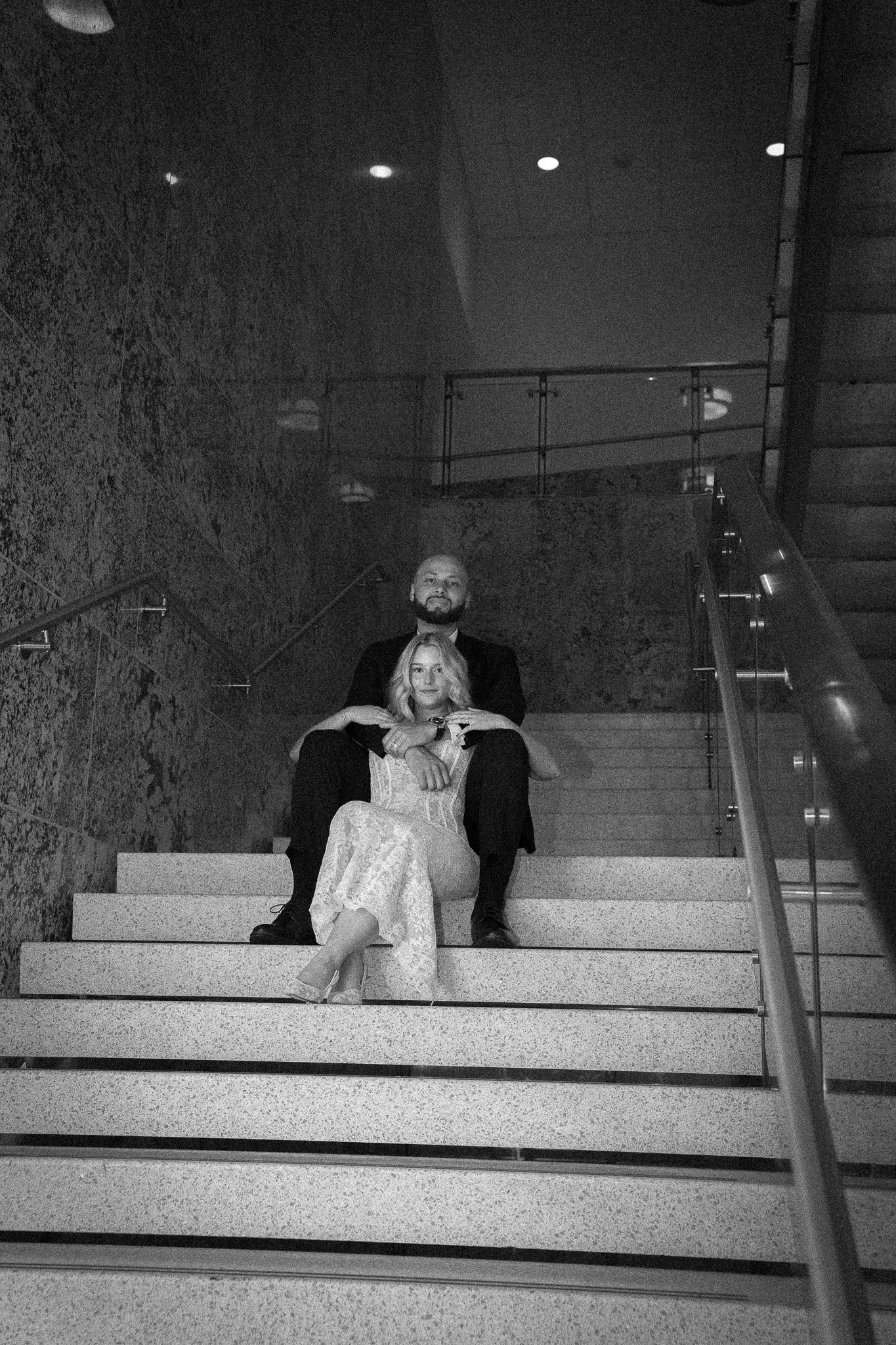 A man and woman sitting on stairs, with the man behind the woman, in black and white.