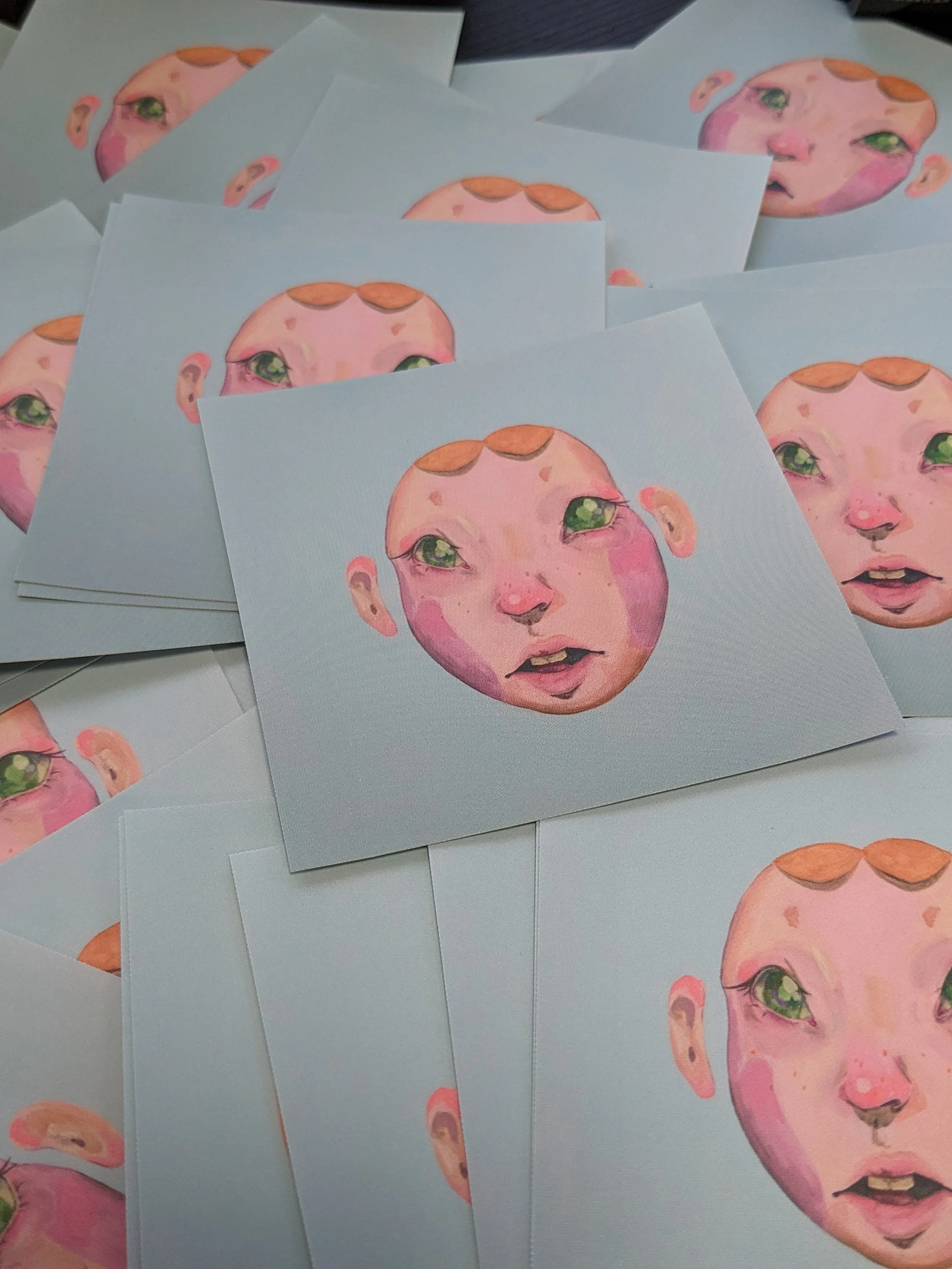 Multiple stickers of a watercolor-style face of a young child with freckles, green eyes, and short orange hair, arranged in a scattered pattern.