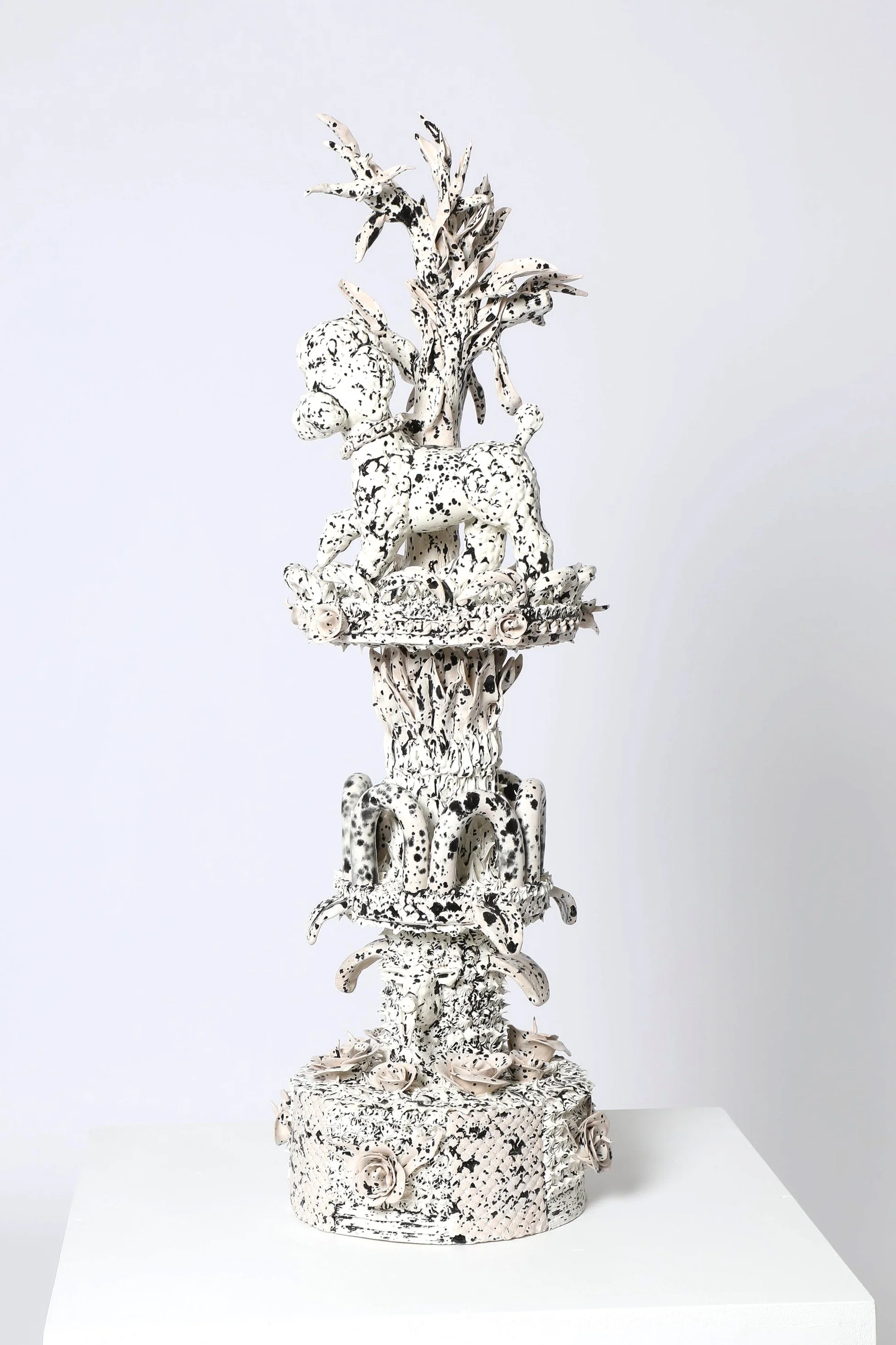 Une sculpture en céramique blanche avec des taches noires représentant un caniche  sur un arbre, avec plusieurs roses à la base.