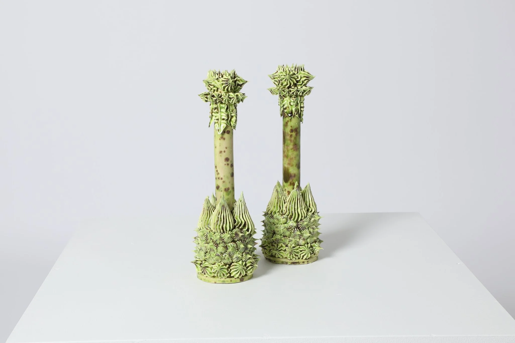 Deux objets sculptés ressemblant à des décors naturels avec des éléments en forme de pointes et de spirales, de couleur verte avec des touches violettes, placés sur une surface blanche.