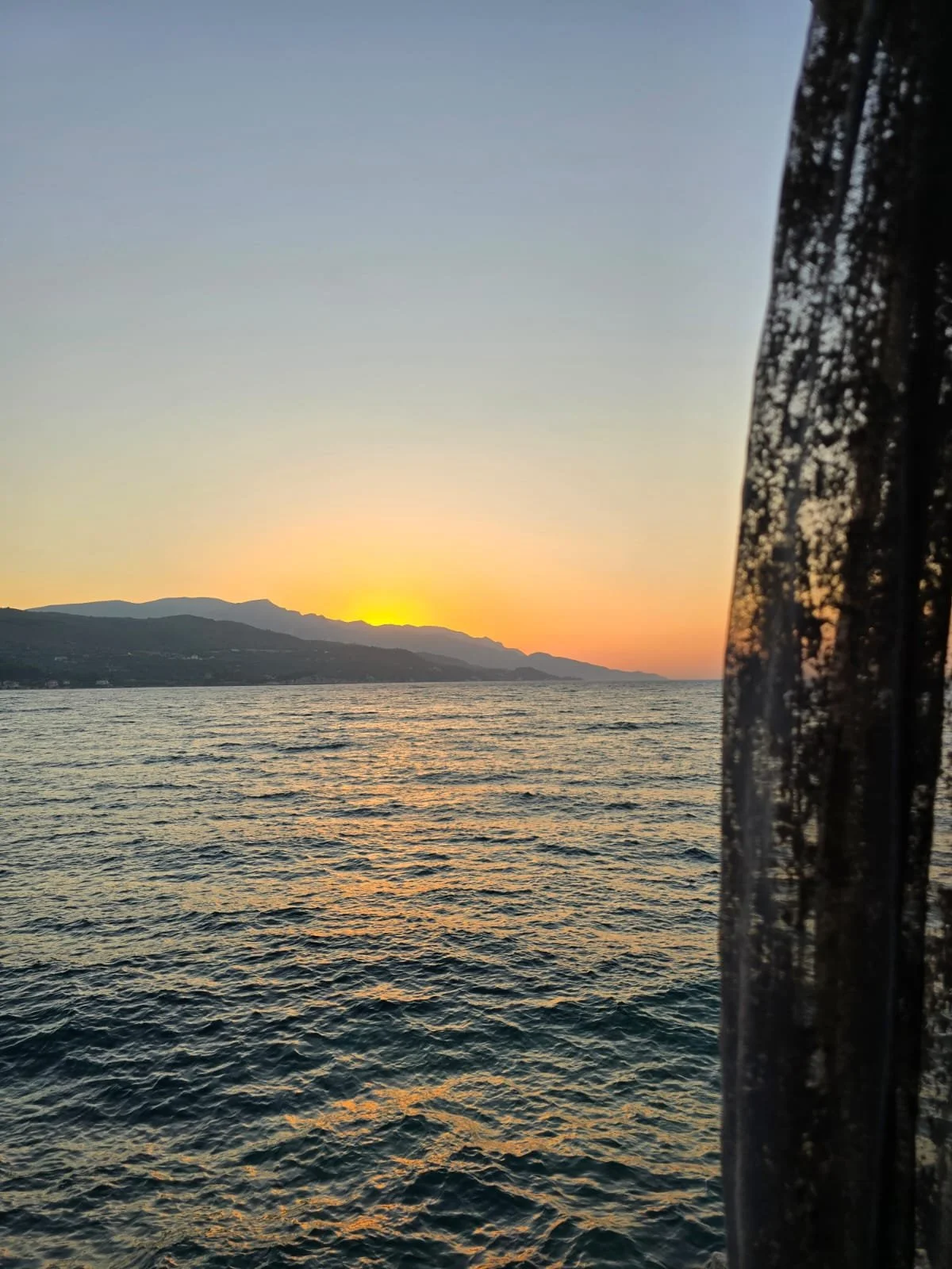 Zonsondergang boven de zee met bergen op de achtergrond en een gordijn aan de rechterkant.