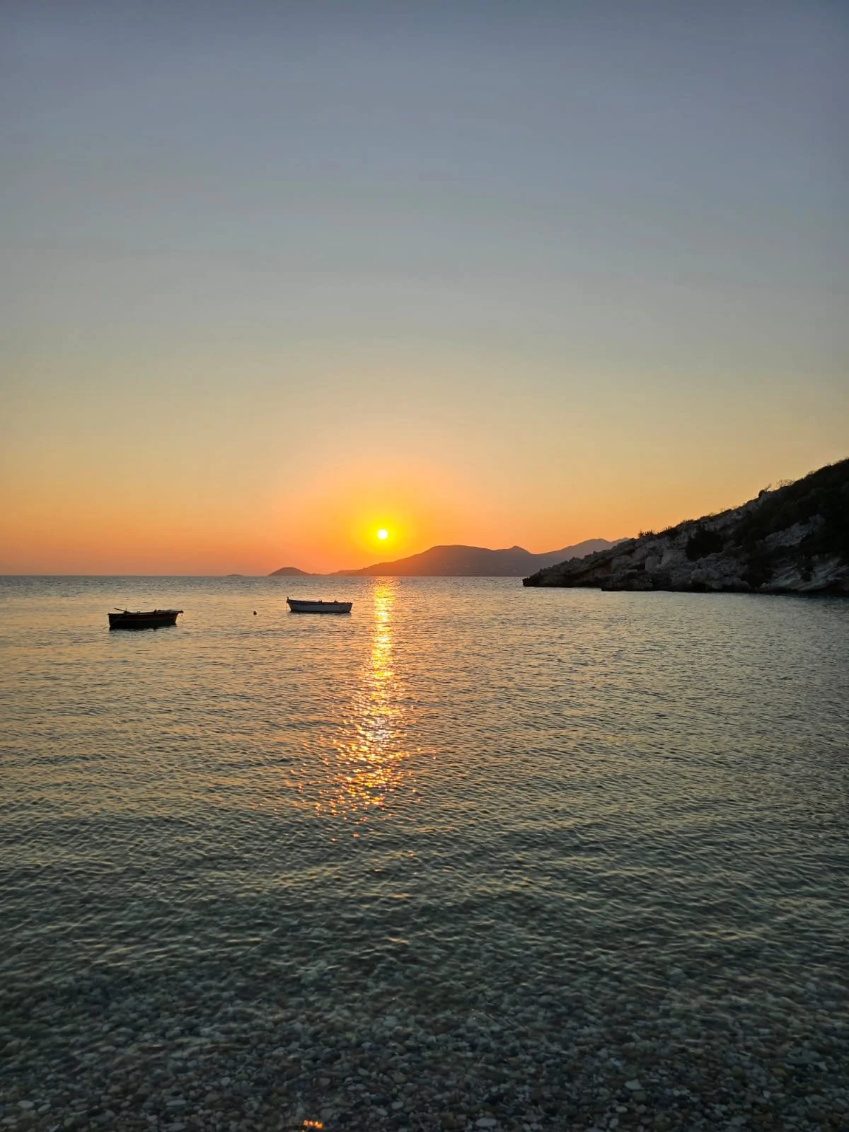 Zonsondergang boven de zee met twee kleine boten en bergen op de achtergrond.