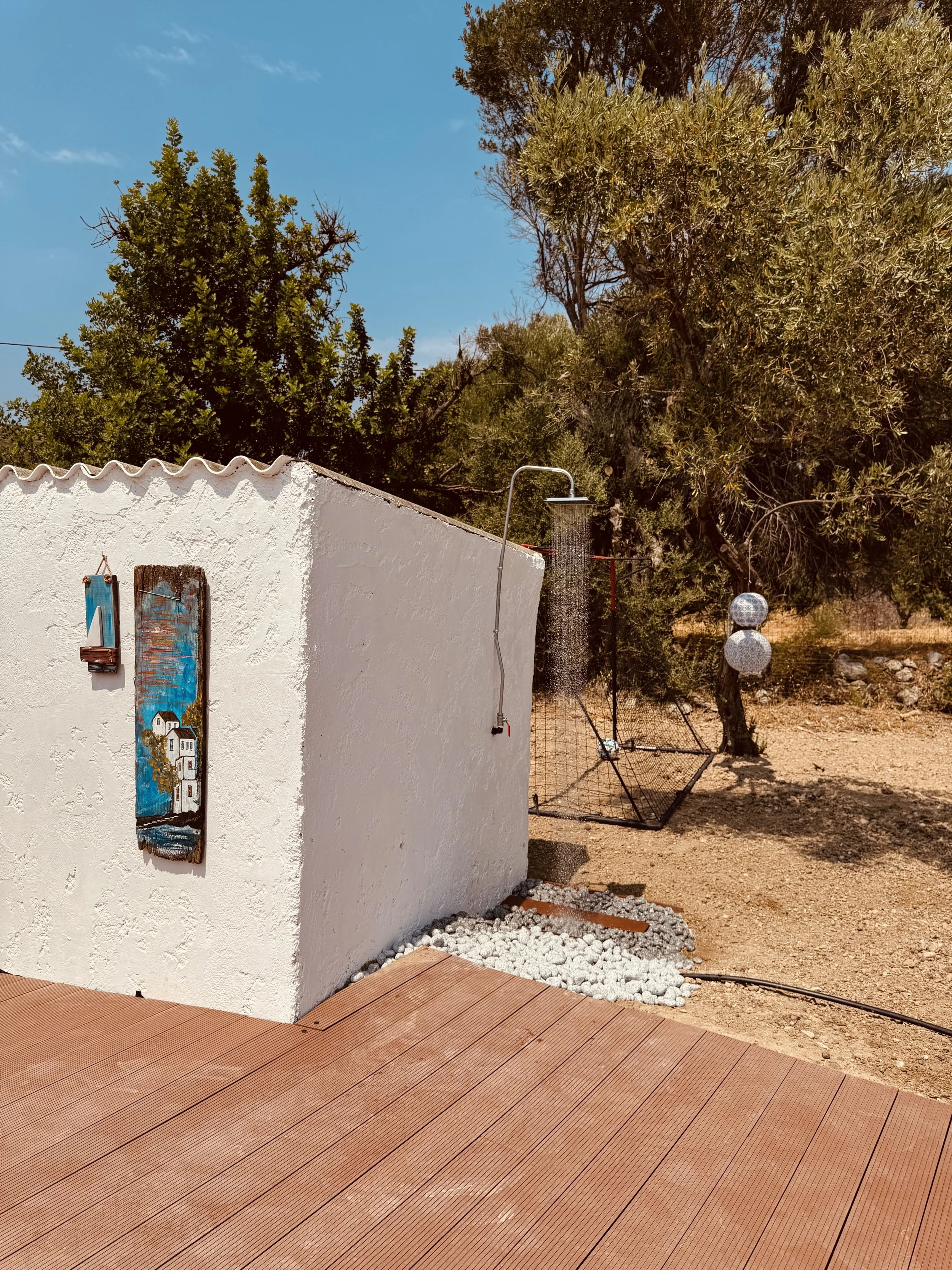 Een witte muur met schilderijen en buiten douchekop met een tuin en bomen op de achtergrond.