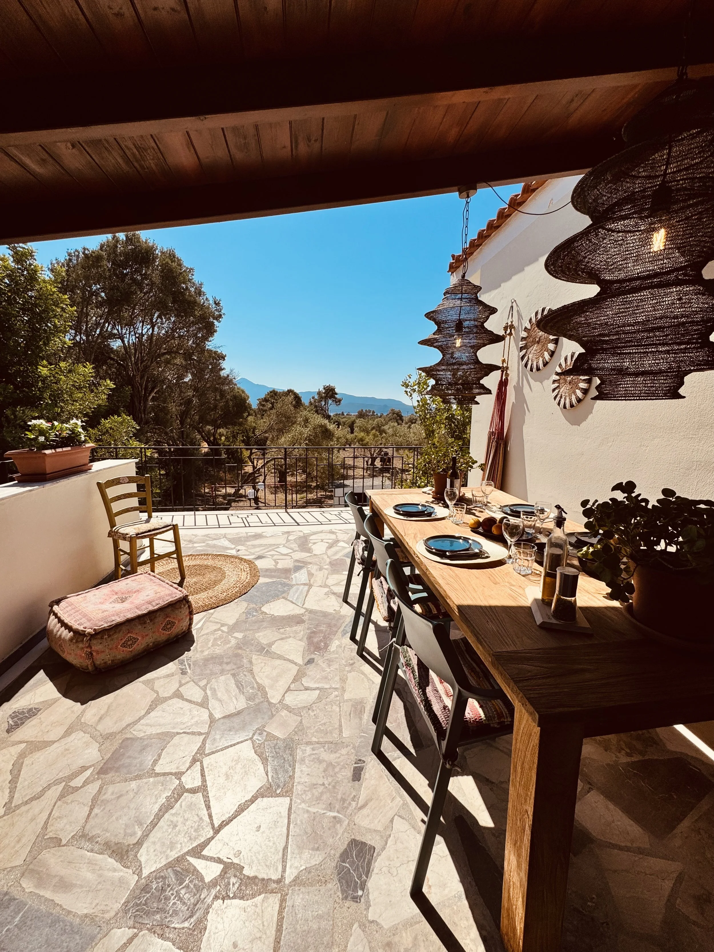 Zomers balkon met eettafel, hangende lampen, groene bomen en blauwe lucht.