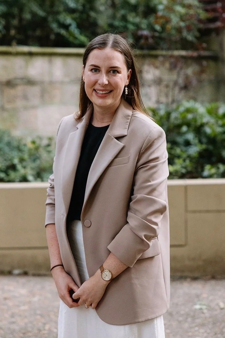 Woman with glasses wearing a black dress, standing outdoors, smiling at the camera.