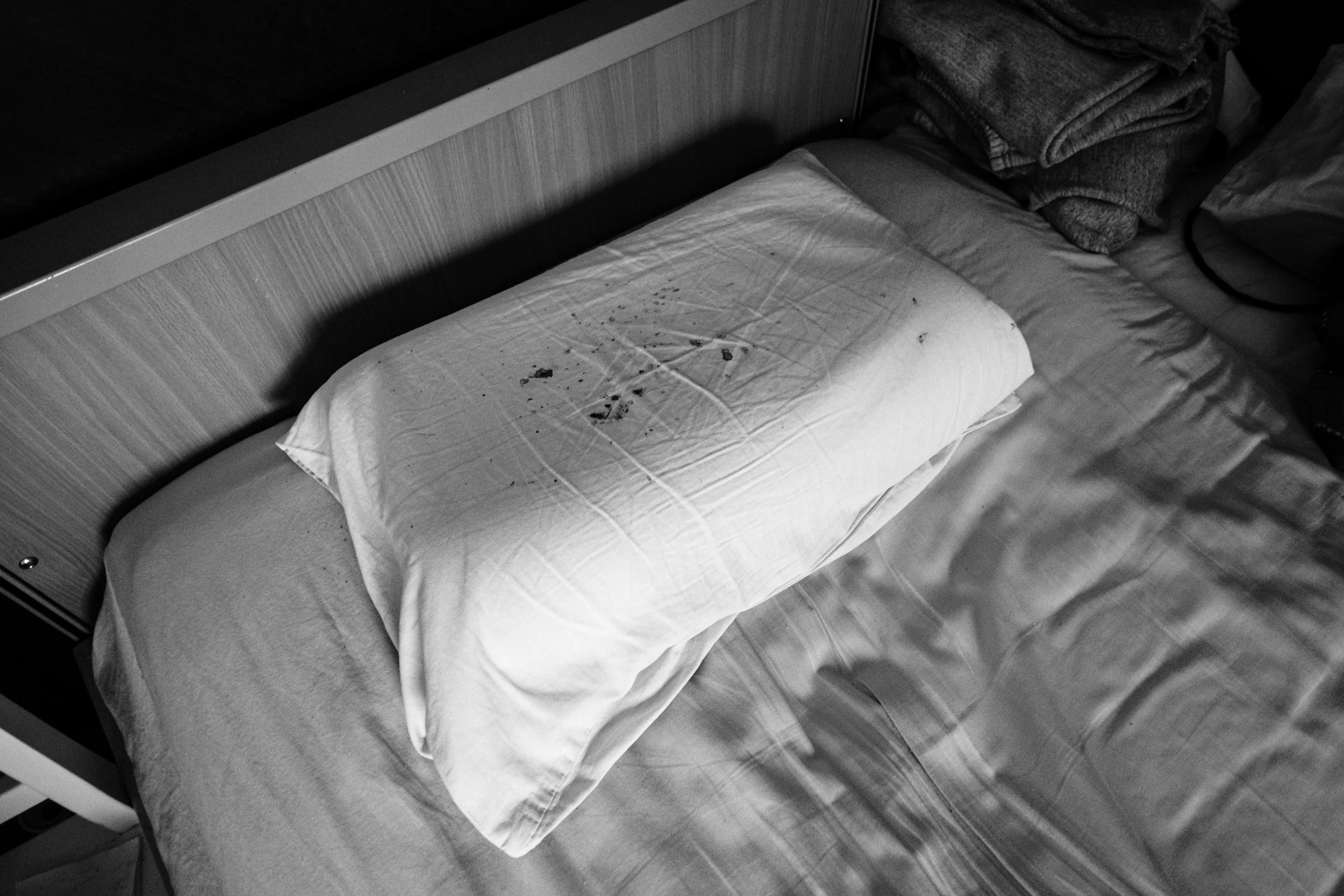 A black-and-white photo of a bloody pillow on a bed in a dim light.