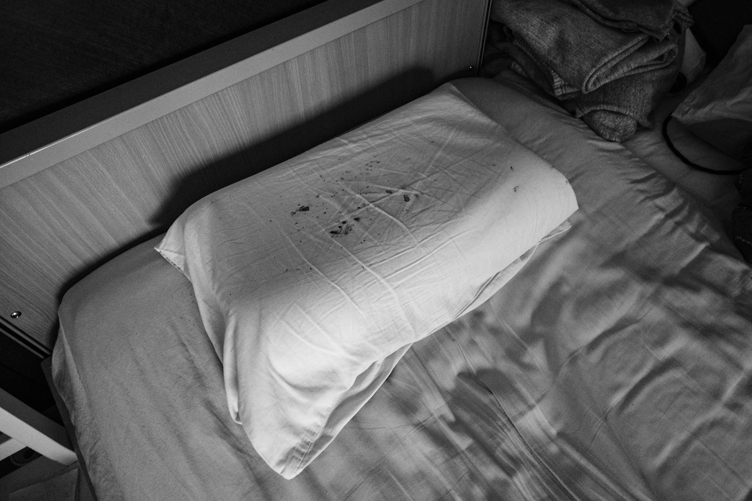 A black and white photo of a bloody pillow on a bed in a dim light.