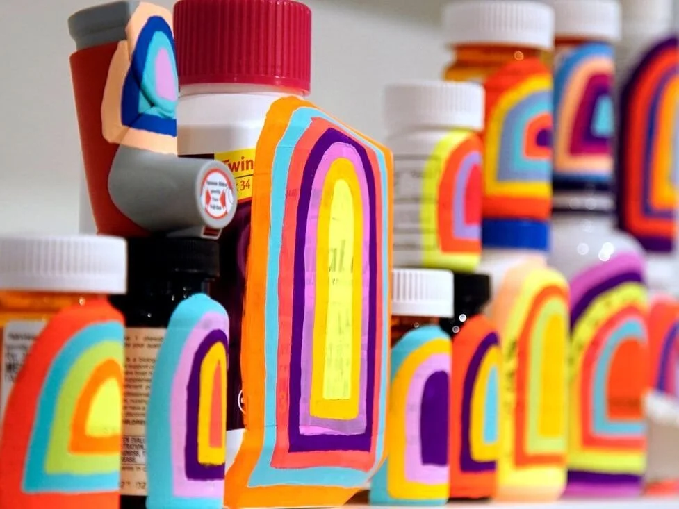 A photograph of a collection of medical bottles, with bright multi-colored archways painted on them.
