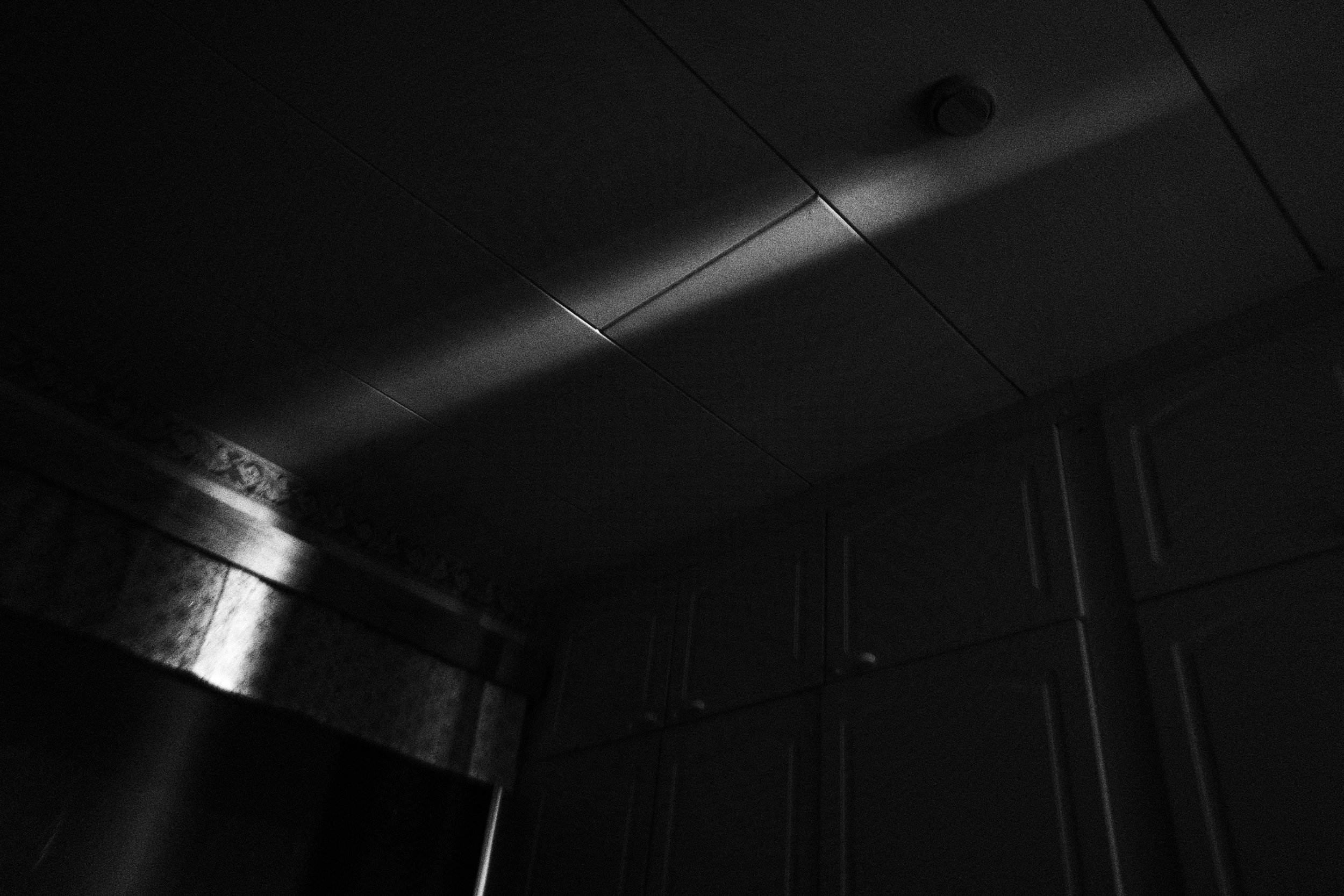 A black and white high contrast photograph showing a ray of light against the ceiling of a dark bedroom.